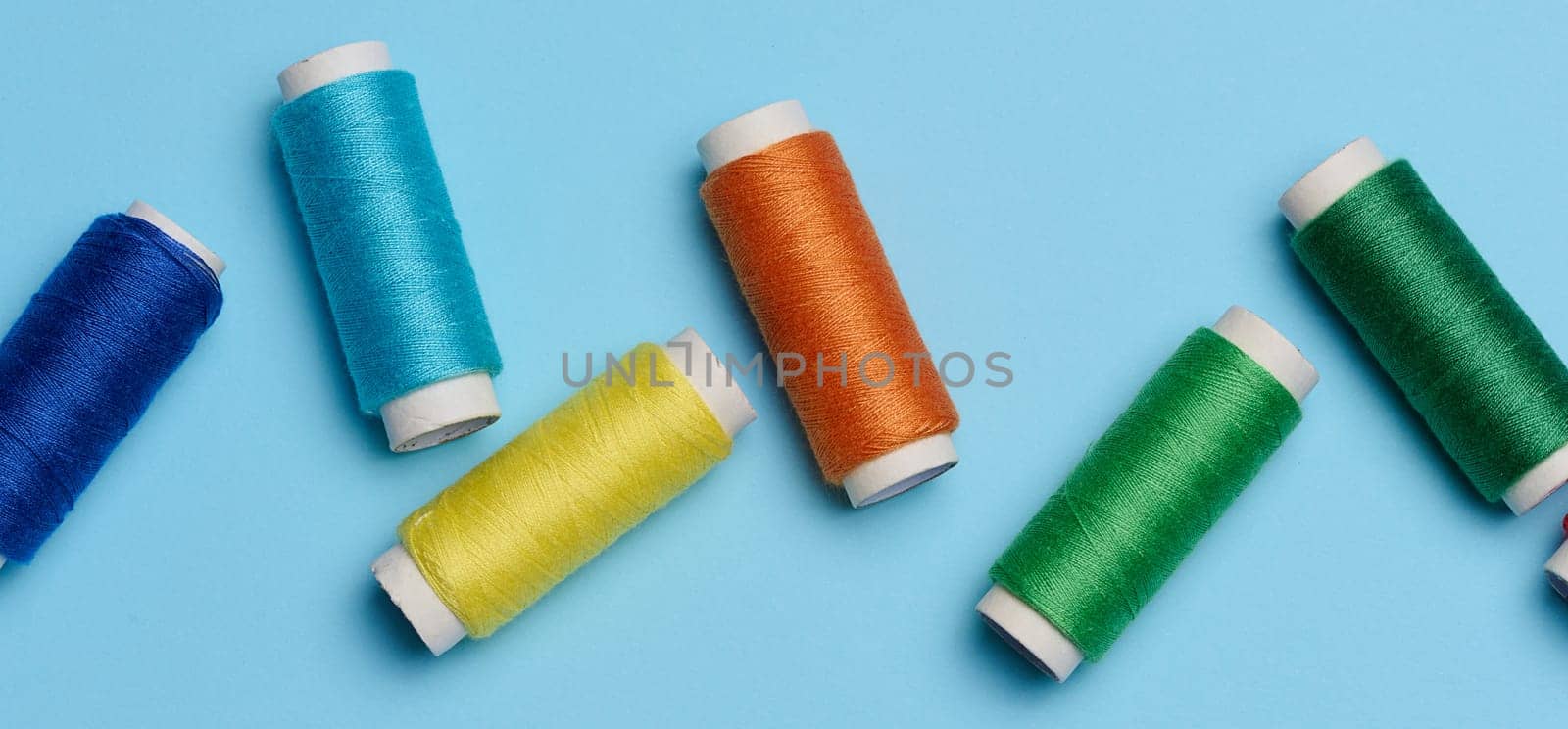Multicolored spools of sewing threads on a blue background, top view by ndanko