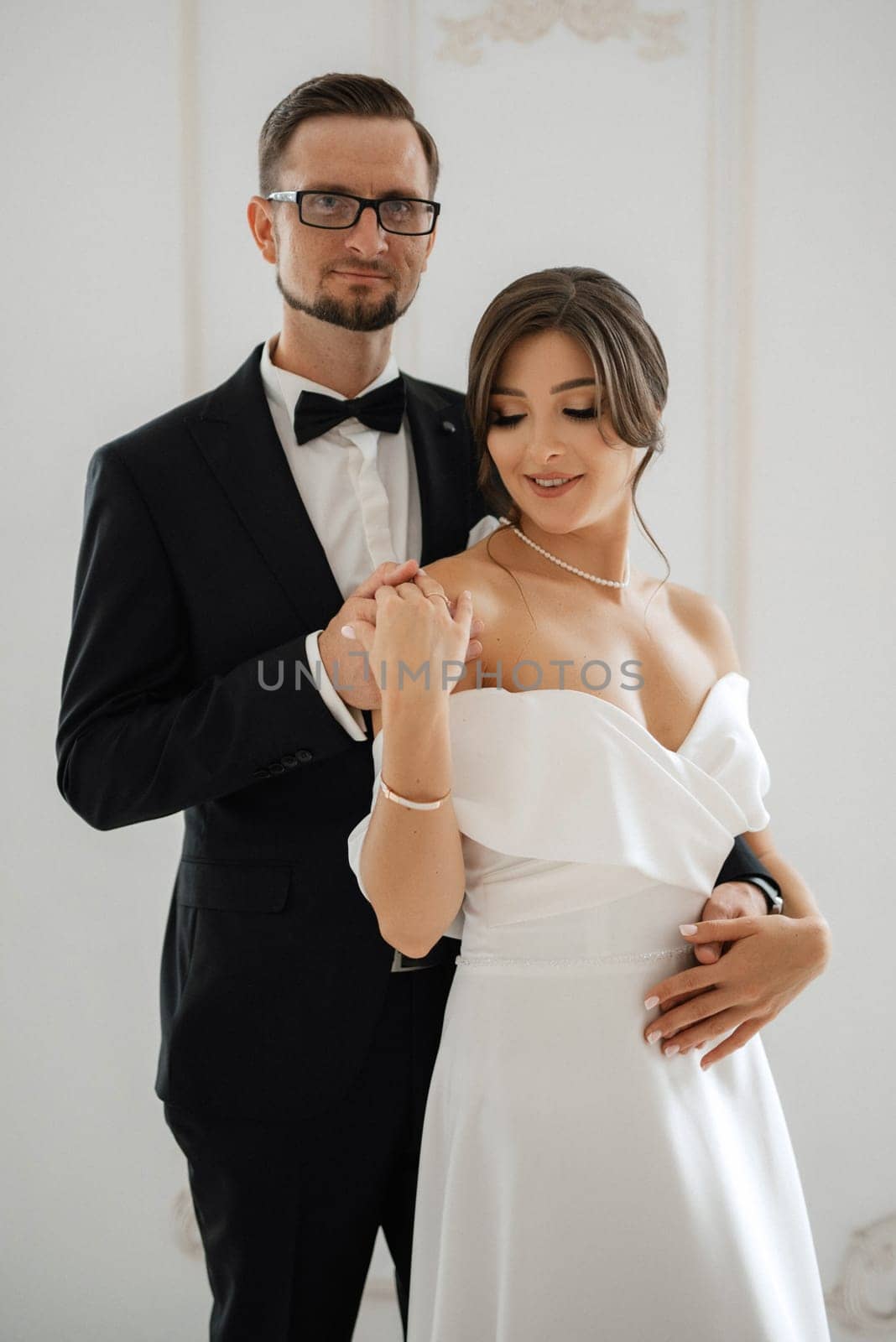 groom in a black suit with a bow tie and the bride in a tight white dress in a bright studio