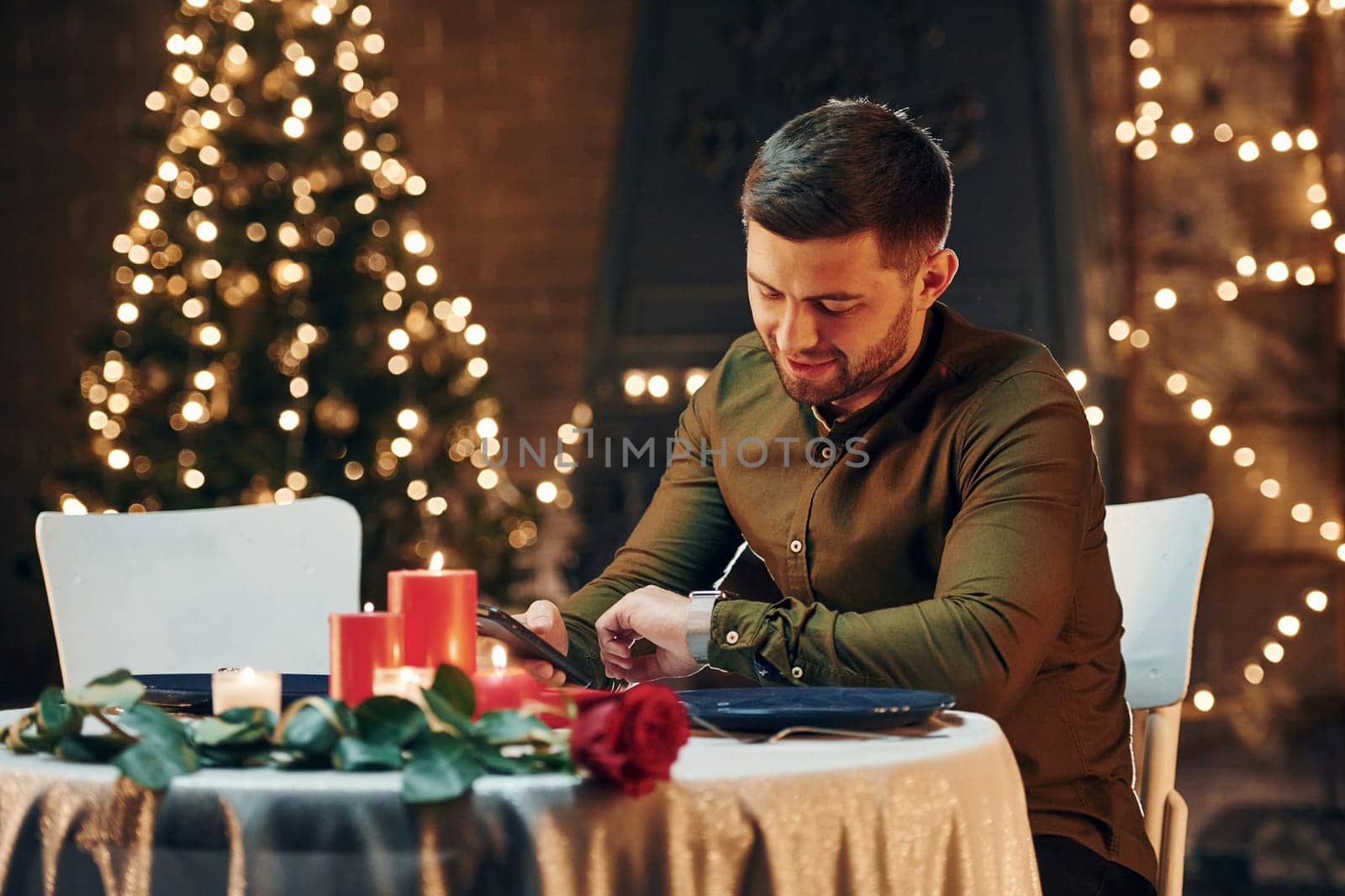 Young handsome man sits by the table and waits for girlfriend for romantic dinner in restaurant.