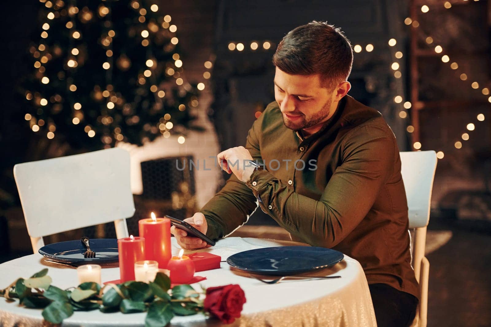 Young handsome man sits by the table and waits for girlfriend for romantic dinner in restaurant by Standret