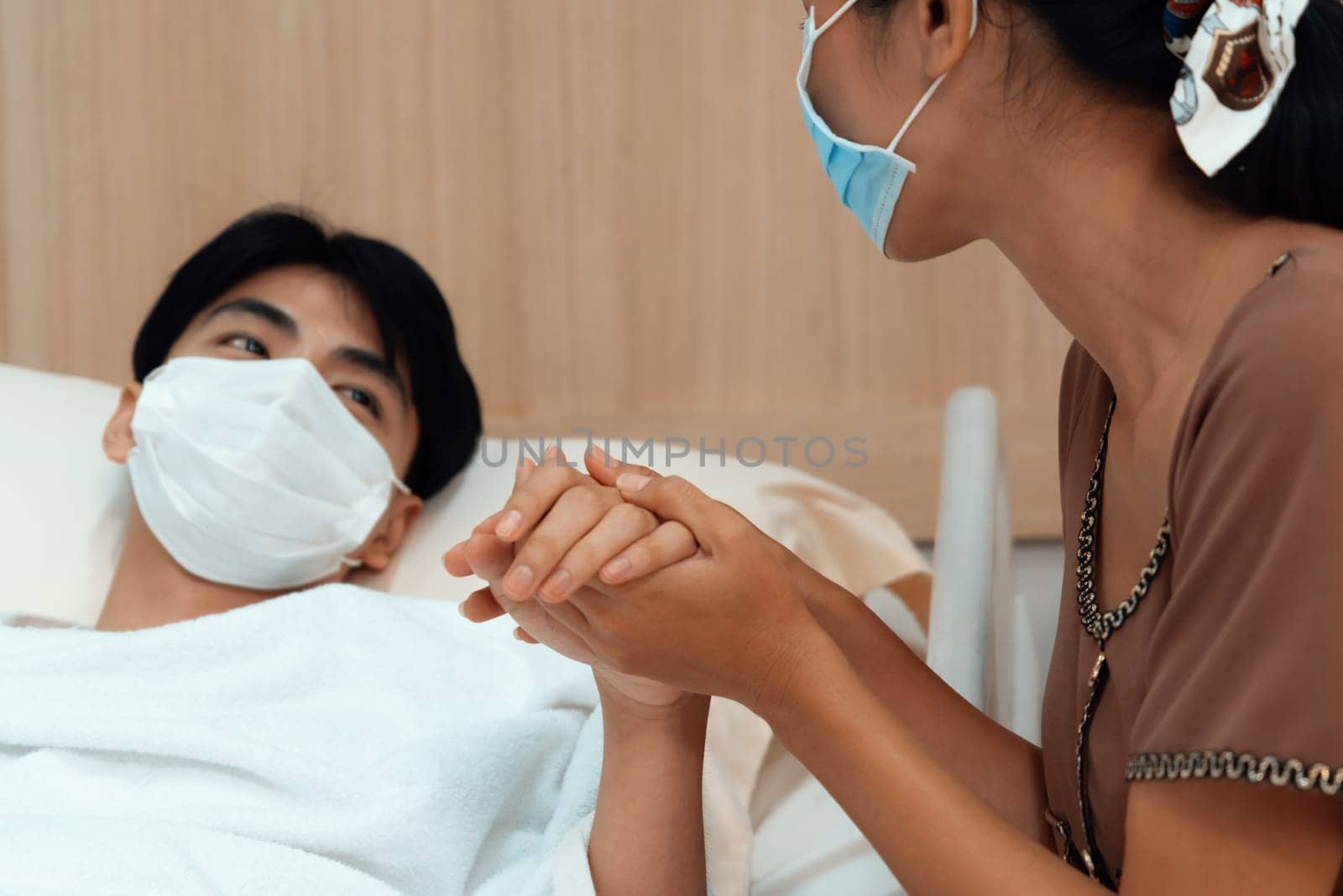 Young patient with attentive visitor and family holding hands in hospital sterile recovery room. The concept of family support for patients receiving hospital care. In-ward medical care and healthcare