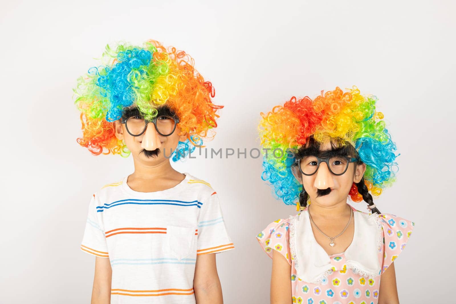 April Fool's Day. Two brothers funny kid boy and little girl clown wears curly wig colorful big nos and glasses and has mustache isolated on white background, Happy children festive decor