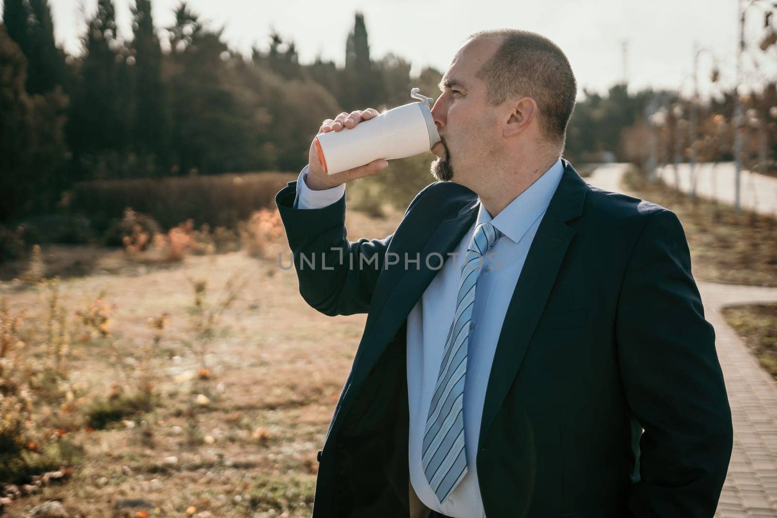 Mature entrepreneur drink coffee in autumn park. Senior executive rest in city park.