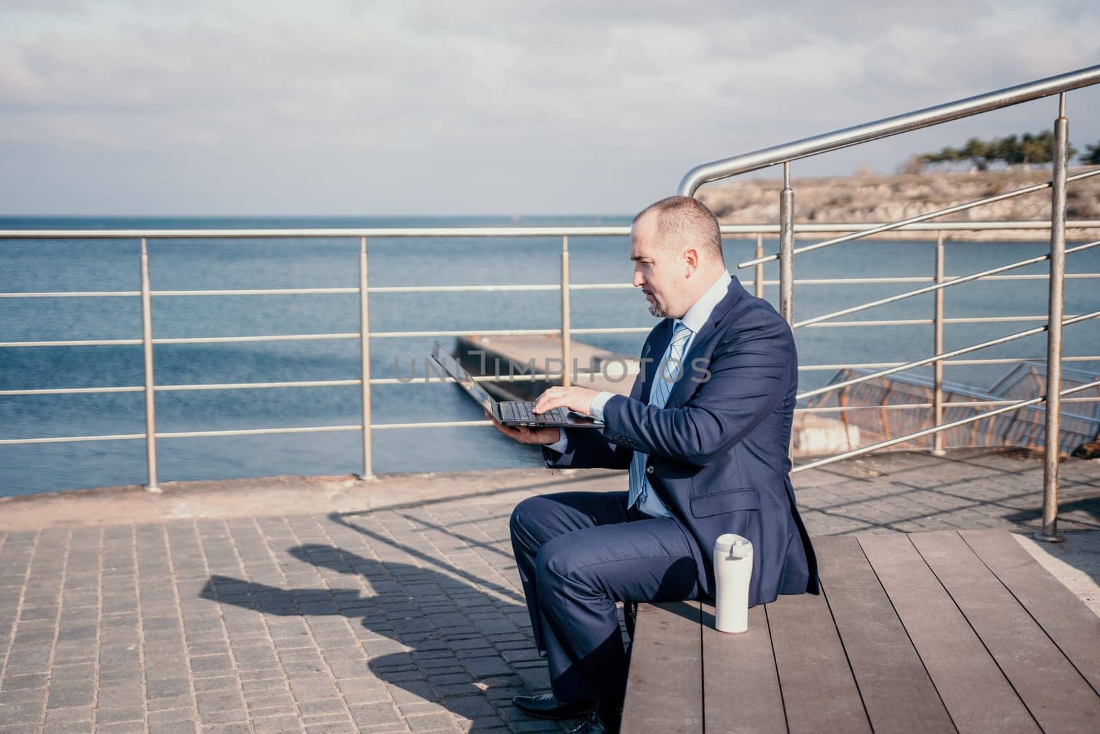 Digital Nomad, a young tattooed man working remotely online, typing on a laptop keyboard while sitting on a beach at sunset. Working remotely on vacation, running an online business from a distance