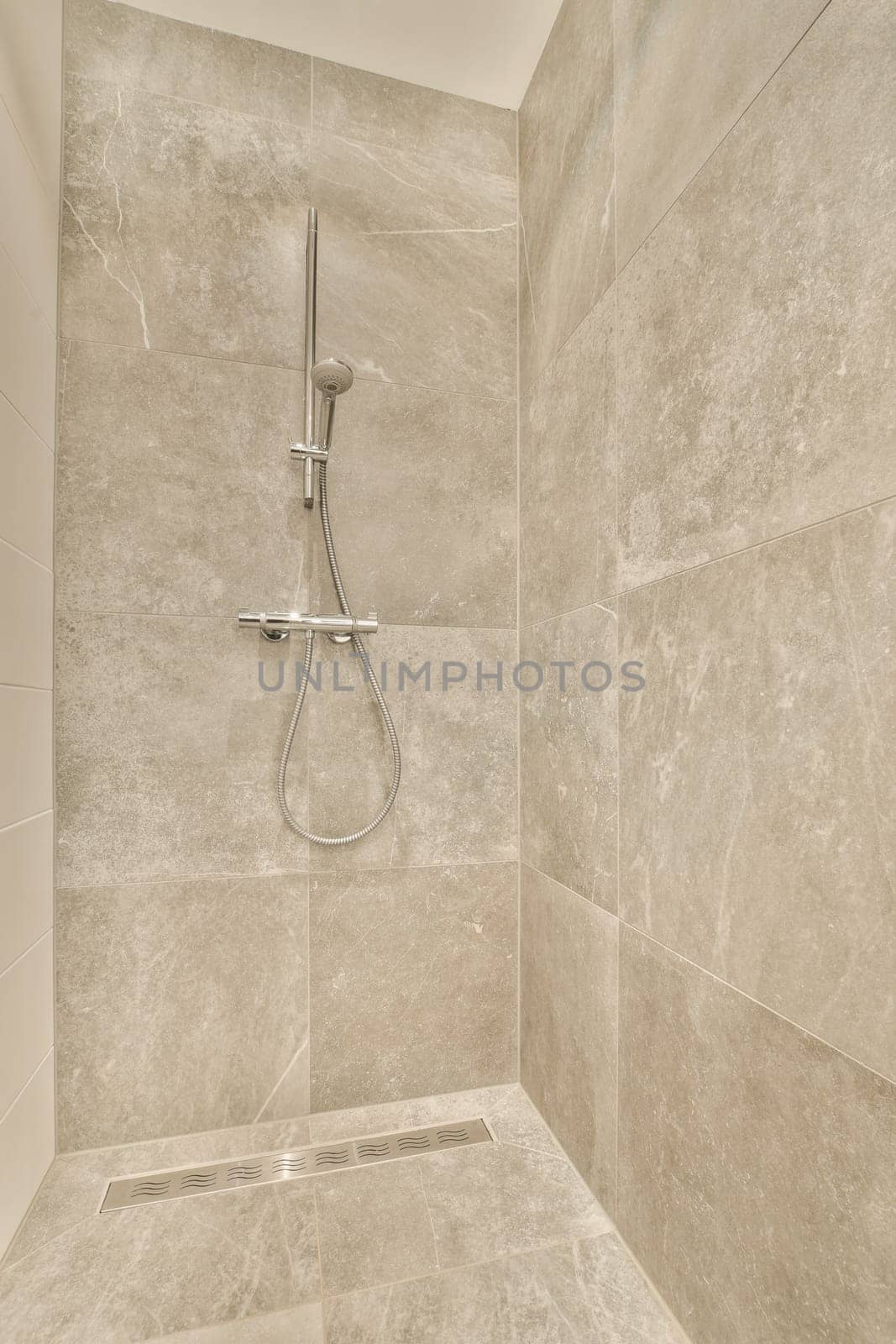 a shower in a bathroom with marble tiles on the walls and flooring around the shower head, which is attached to the wall