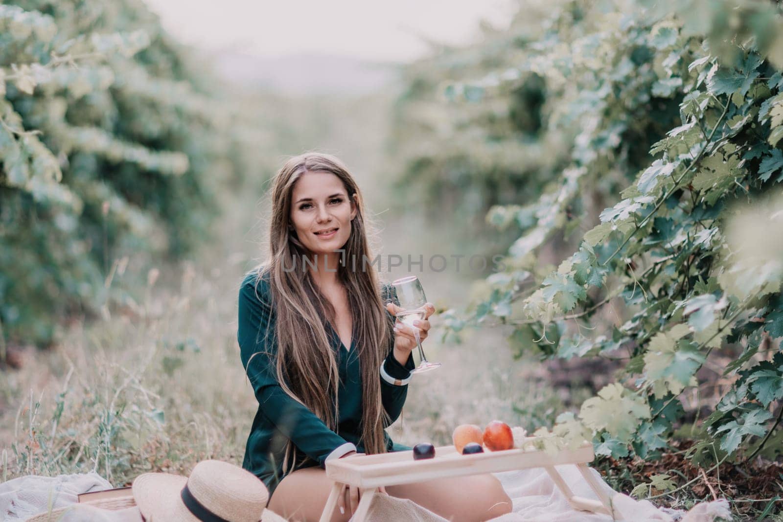 Woman picnic vineyard. Happy woman with a glass of wine at a picnic in the vineyard, wine tasting at sunset and open nature in the summer. Romantic dinner, fruit and wine. by panophotograph