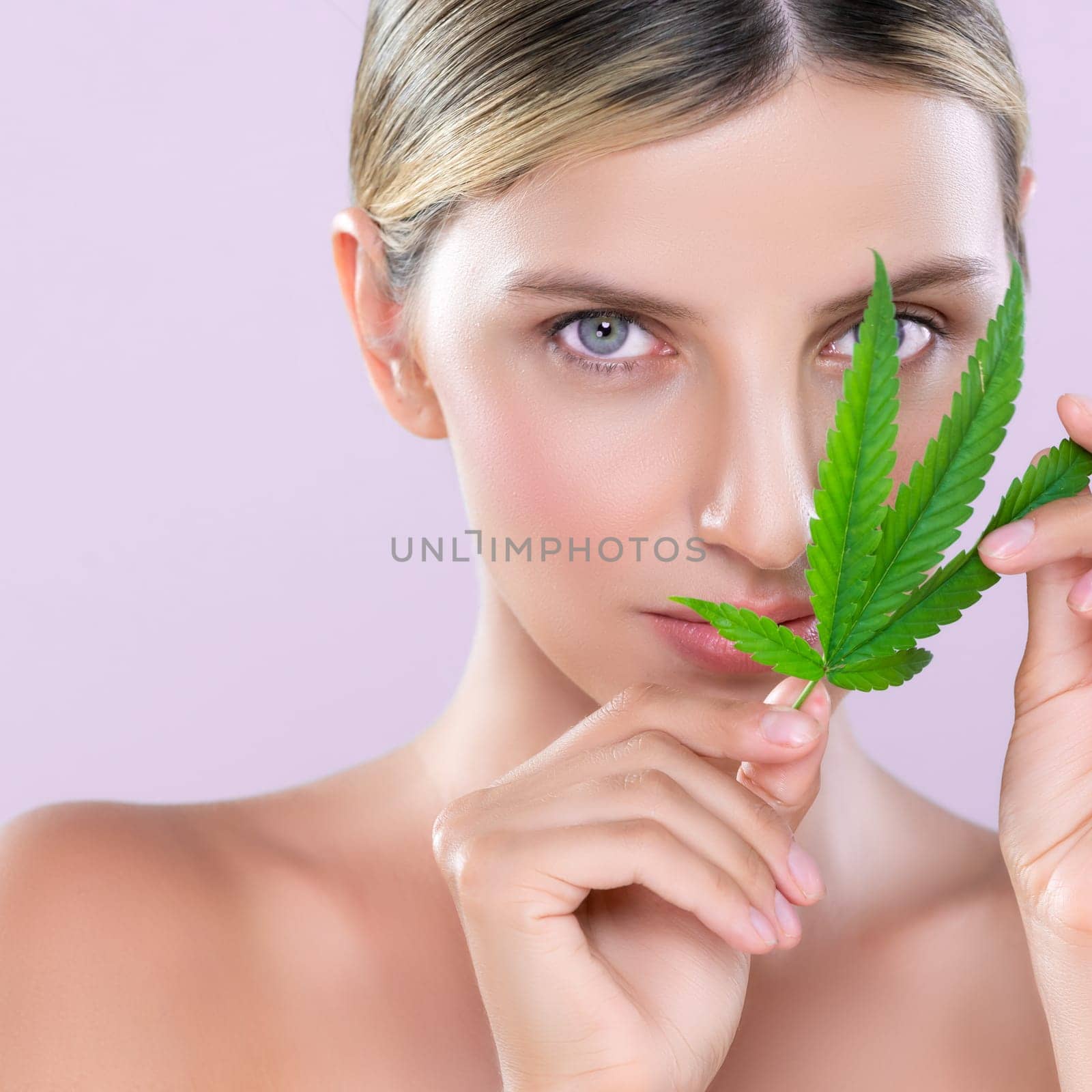 Closeup alluring beautiful woman model portrait holding green leaf as concept for cannabis skincare cosmetic product for perfect skin freshness treatment in isolated pink background.