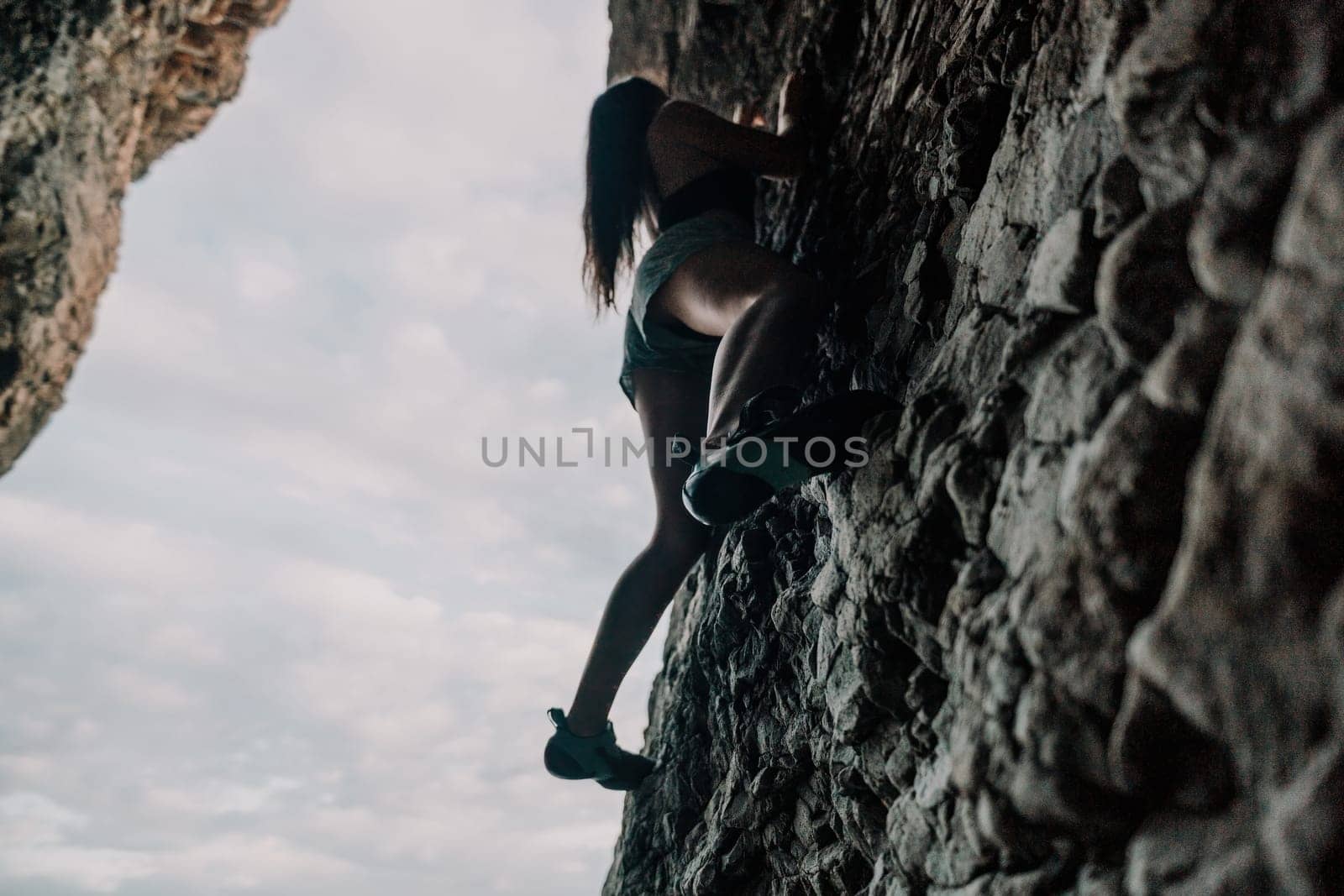 A girl climbs a rock. The athlete trains in nature. Woman overcomes difficult climbing route. Extreme hobby. Tourist woman rock climber hiking on mountains rocks over beautiful sea coast