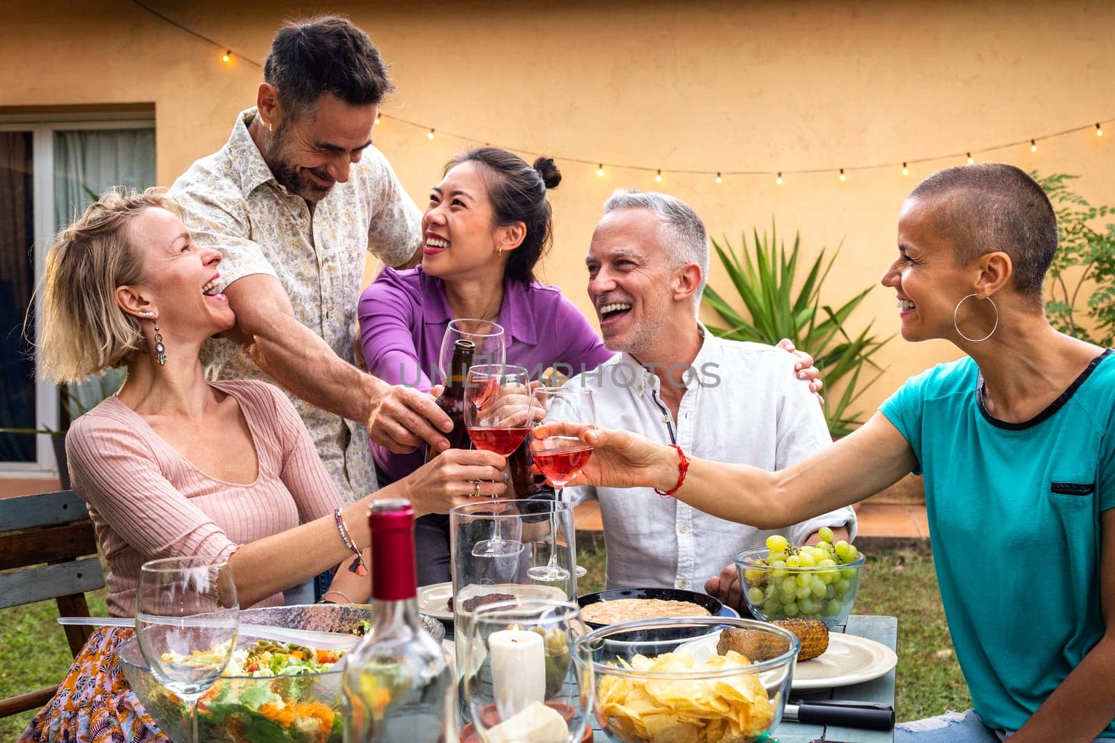 Group of friends celebrating life, toasting with wine, laughing and having fun during barbecue garden dinner party. Lifestyle.