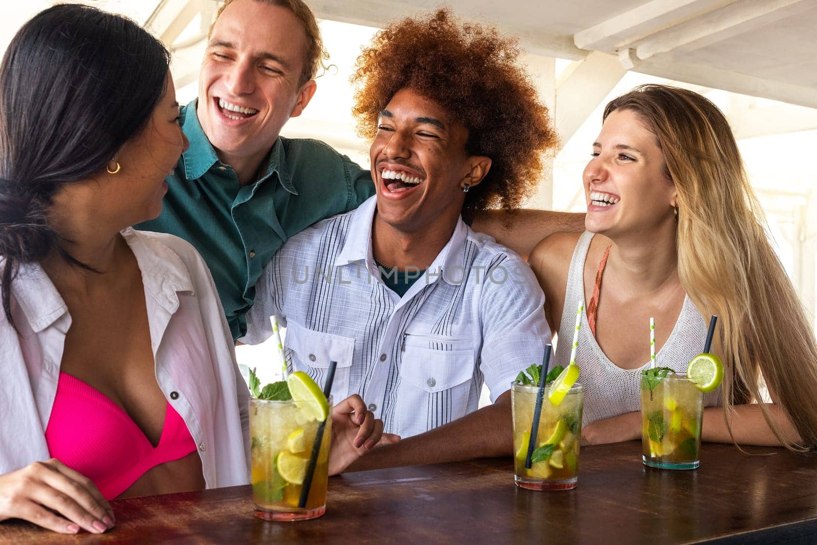 Group of happy multiracial friends laughing and having fun drinking mojito cocktails at a beach bar. by Hoverstock