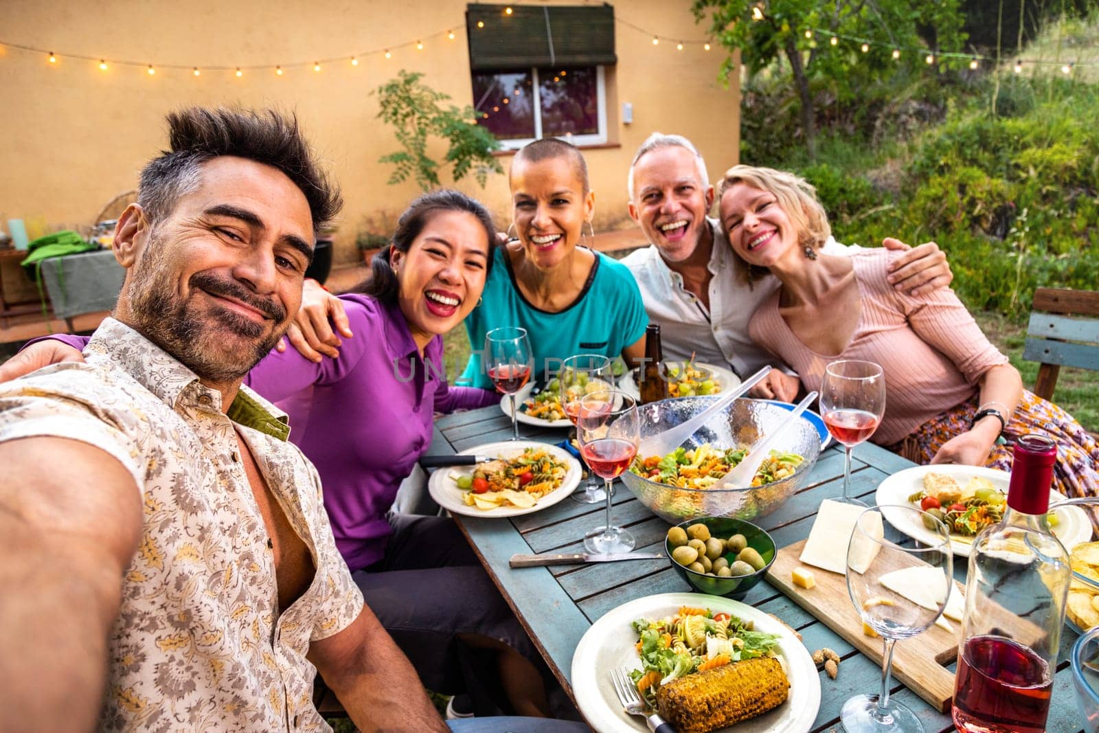 Happy group of friends laughing taking selfie during barbecue dinner party outdoors. by Hoverstock