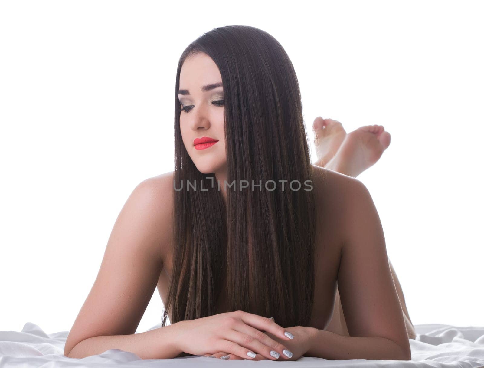 Beautiful brunette woman with long hair lying on bed. Isolated on white