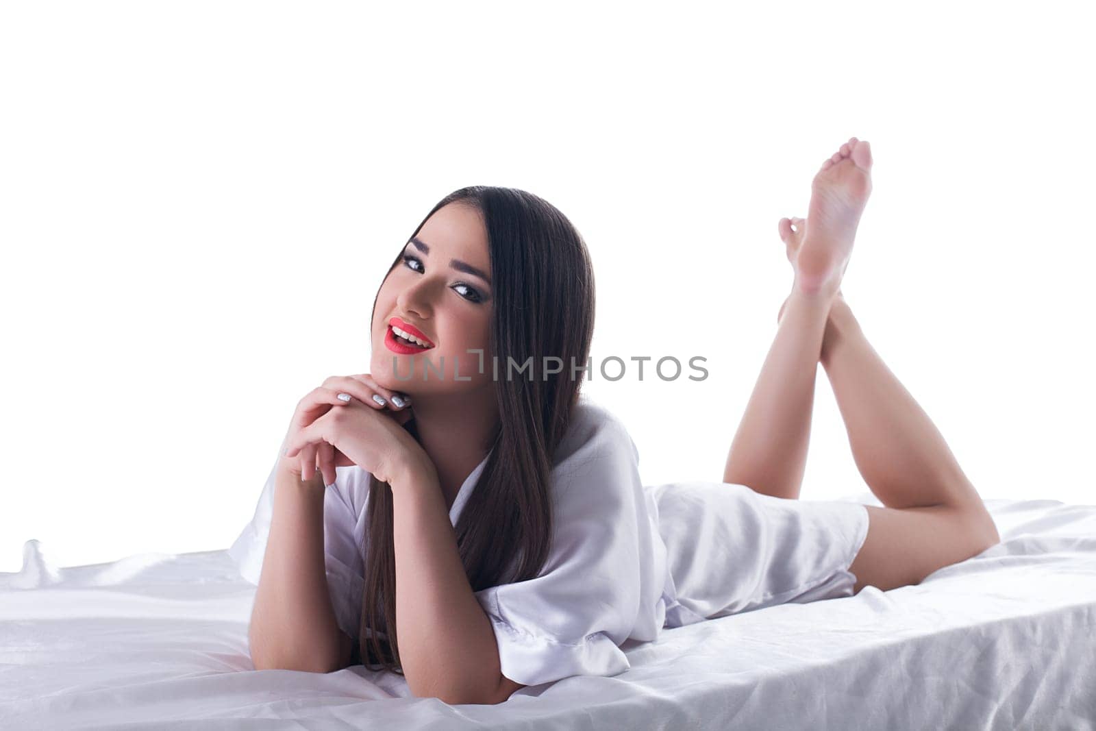 Pretty brunette woman with long hair lying on bed. Isolated on white