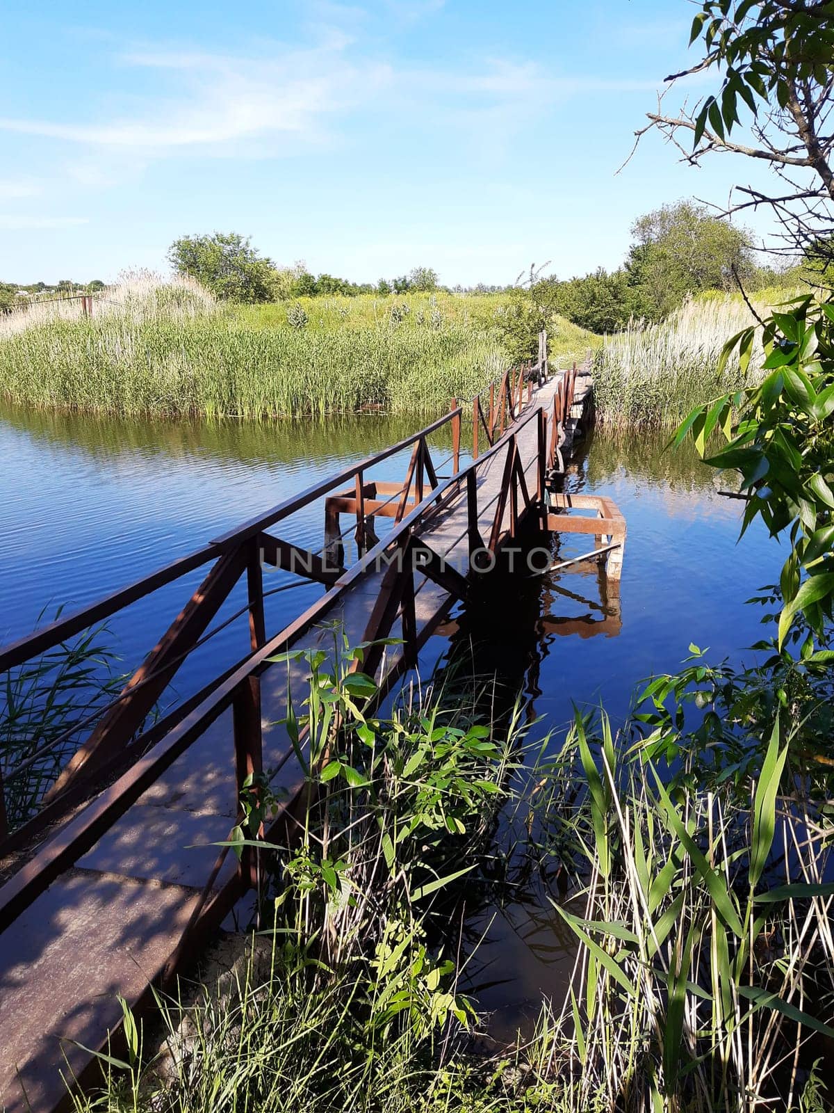 Old ruined iron bridge across the river on a summer day.