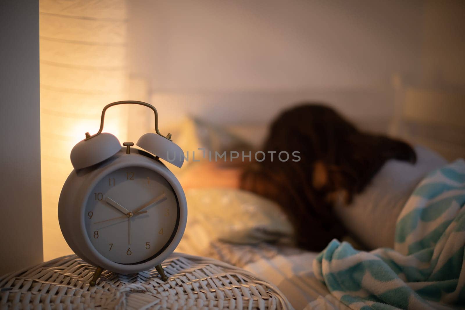 The alarm clock stands on the cabinet next to the bed in which the woman sleeps with the bedside lamp lit. It is already 10 minutes past 10 o'clock on the clock.