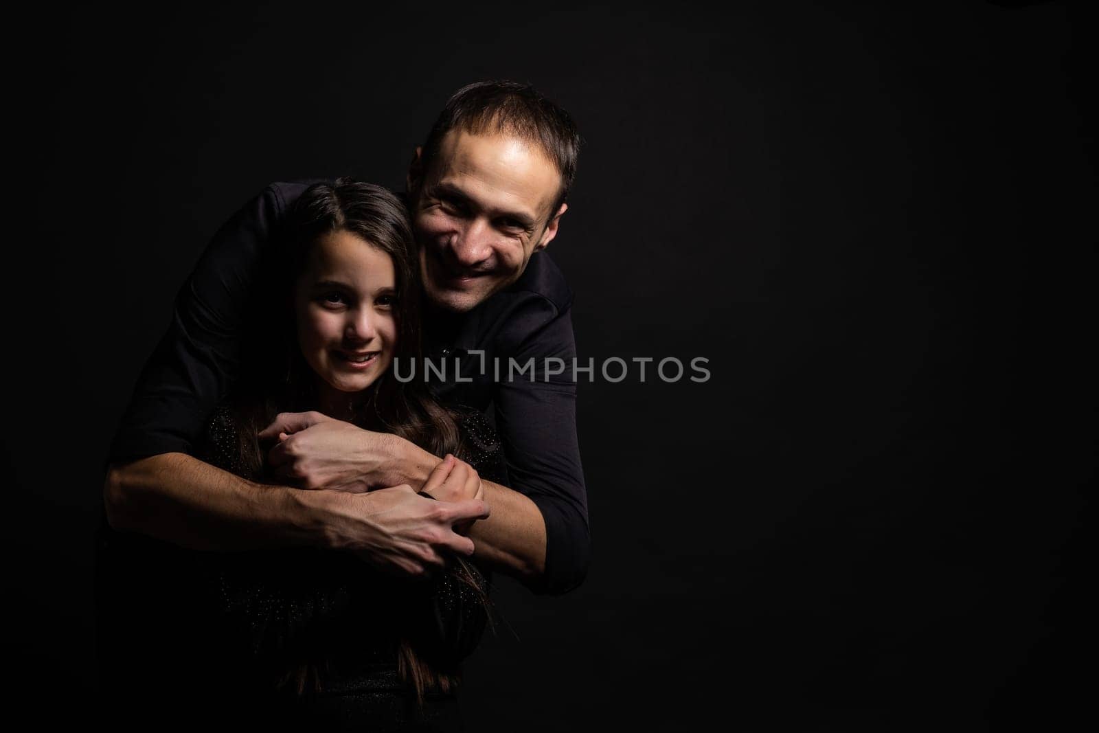 Young dad with a cute emotional daughter on a dark background. Place for your text