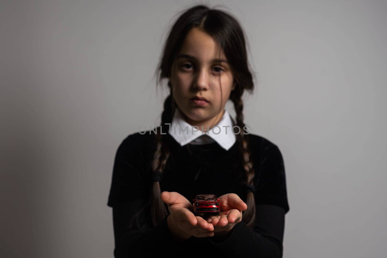 A girl with braids in a gothic style on a dark background with toy car.