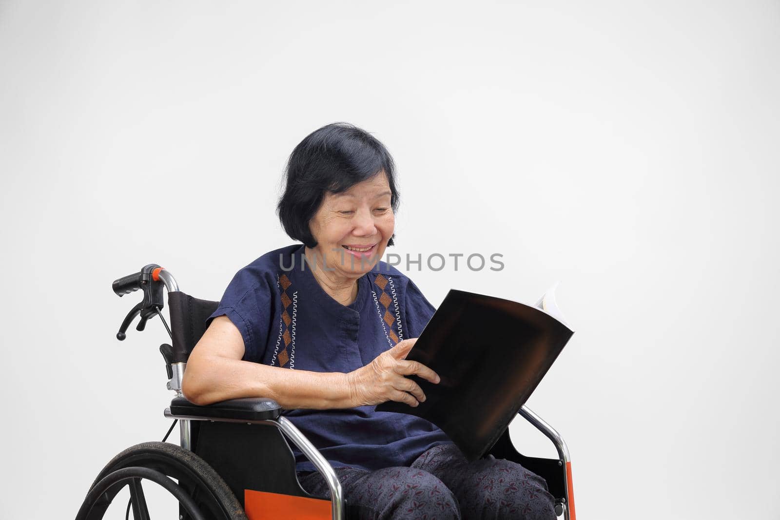 Senior asian woman smiling while reading magazine on white background.