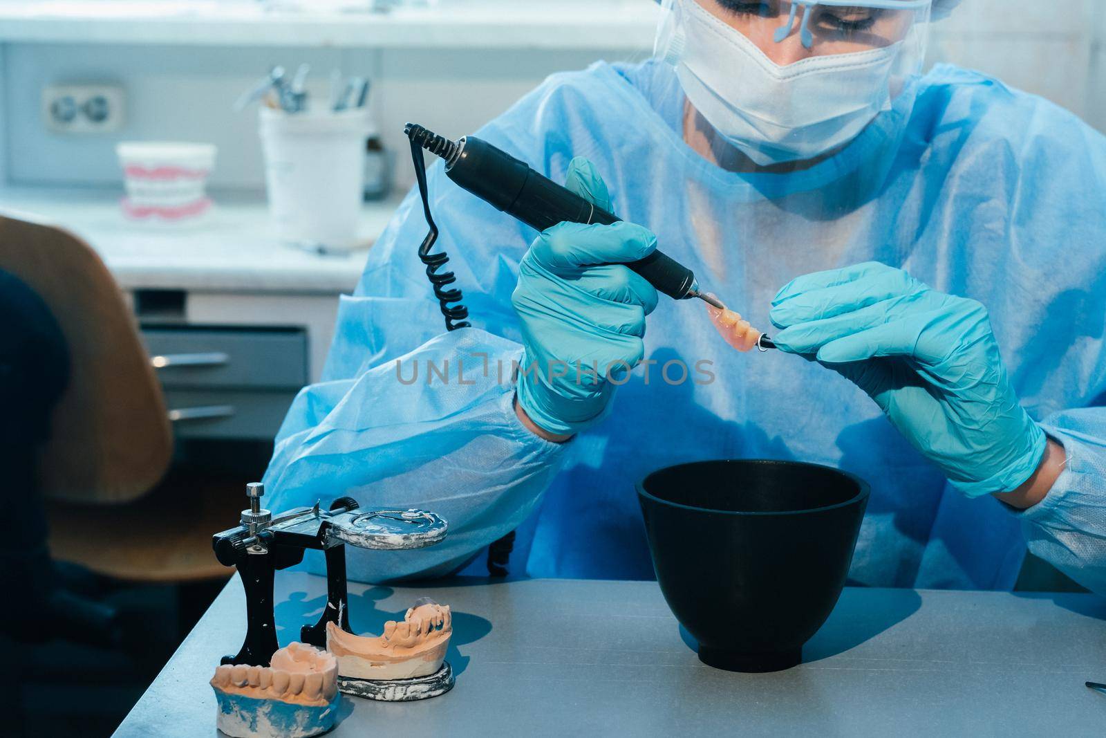 A masked and gloved dental technician works on a prosthetic tooth in his lab by Lobachad