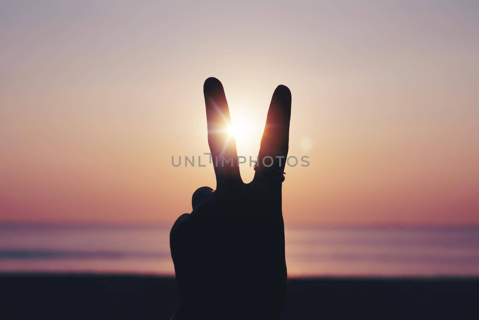 Peace out or fighting metaphor two fingers hand sign in front of a sunset. Happy people enjoying nature. 