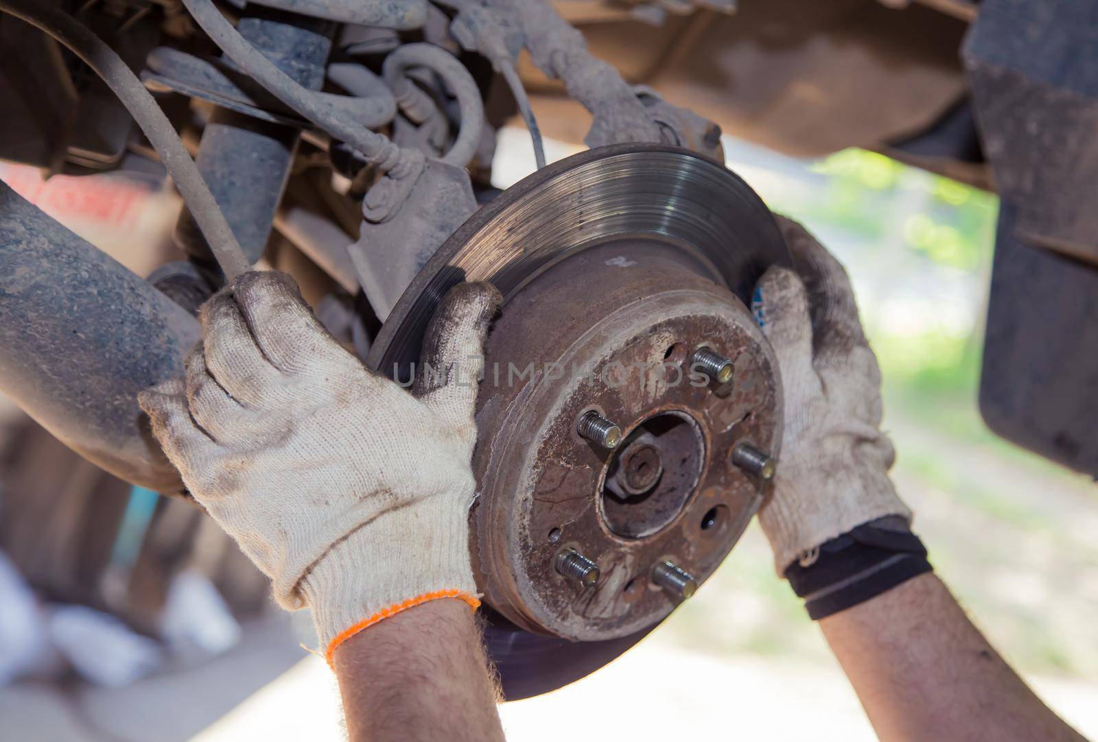 The man's hands remove the worn brake disc from the rear wheel hub. In the garage, a person changes the failed parts on the vehicle. Small business concept, car repair and maintenance service.