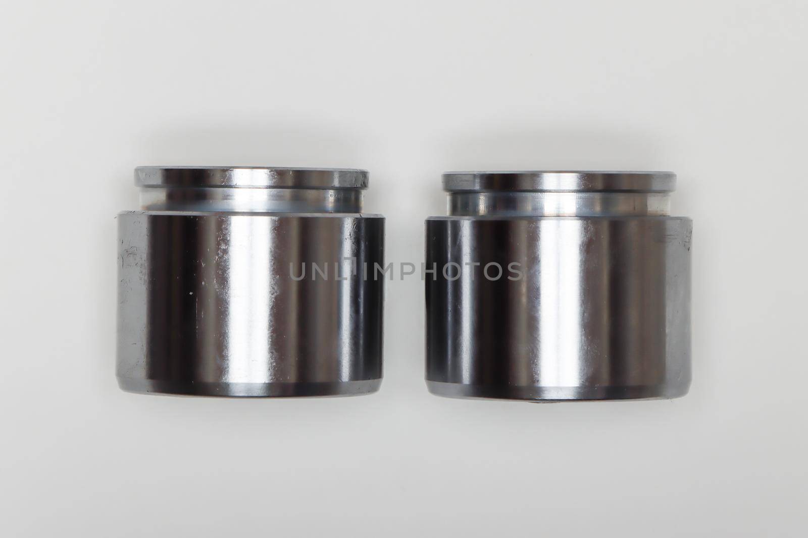 Two metal identical pistons, parts for car repair. A set of spare parts for servicing the braking system of a vehicle. Details on white background, copy space available.