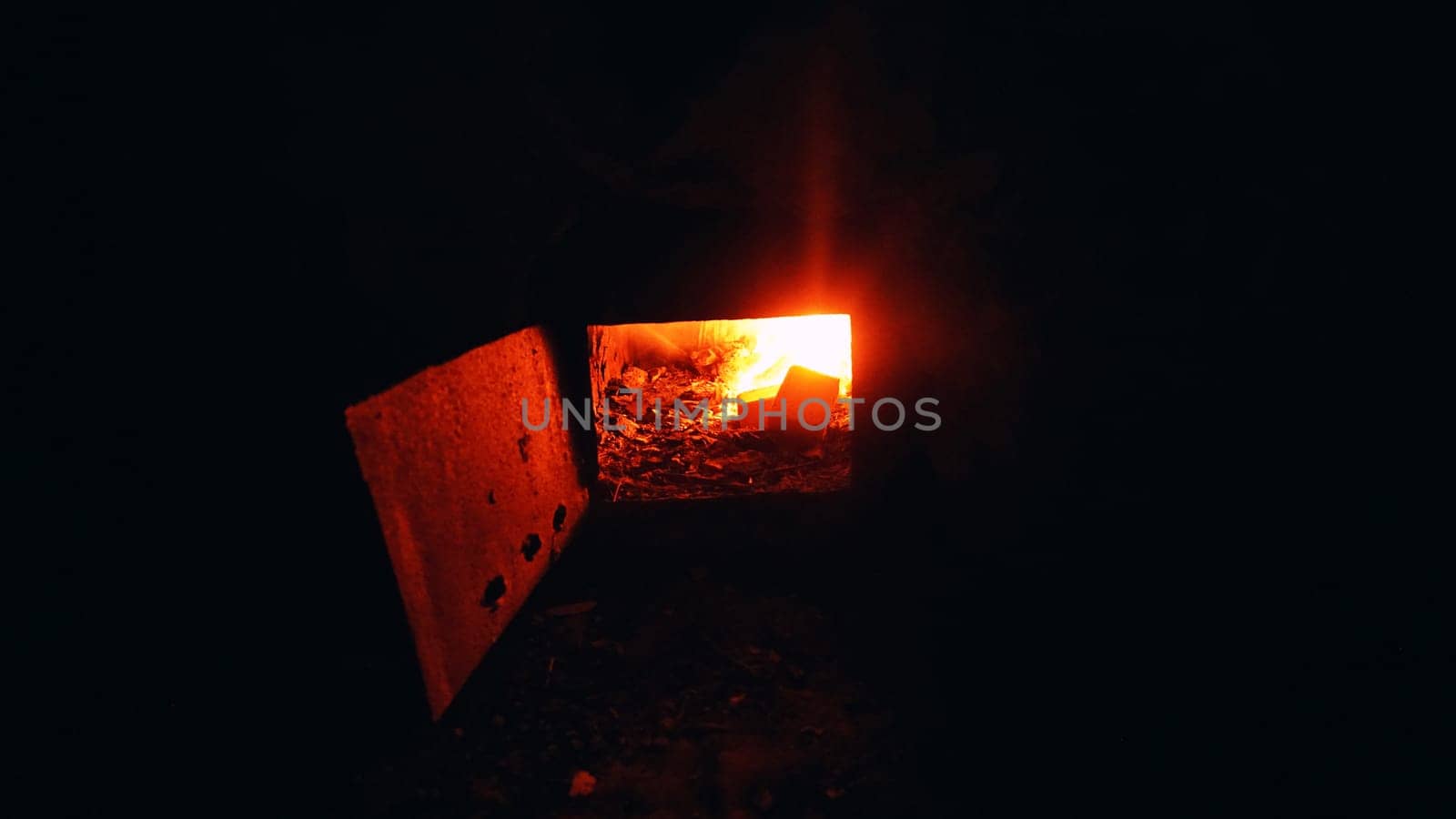 A fire is burning in an old stove in the wall. Rusty metal on the door, damp frozen gray walls. Garbage on the floor. An abandoned hut and a former prison.