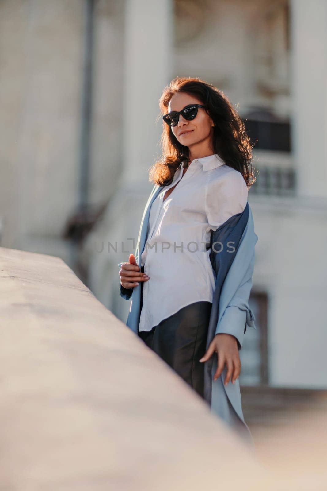 Portrait of a brunette business lady with glasses. Woman walks around the city, lifestyle. She wears a blue cloak, a black leather skirt, and black heeled boots