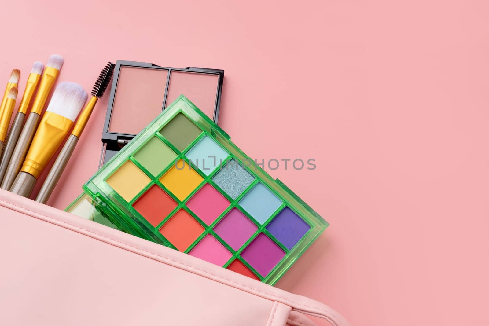 Bright summer eyeshadow palette and makeup products in pink cosmetic bag on pink background. Makeup cosmetics. Colorful colors. Place for text. Flat lay. Top view. layout