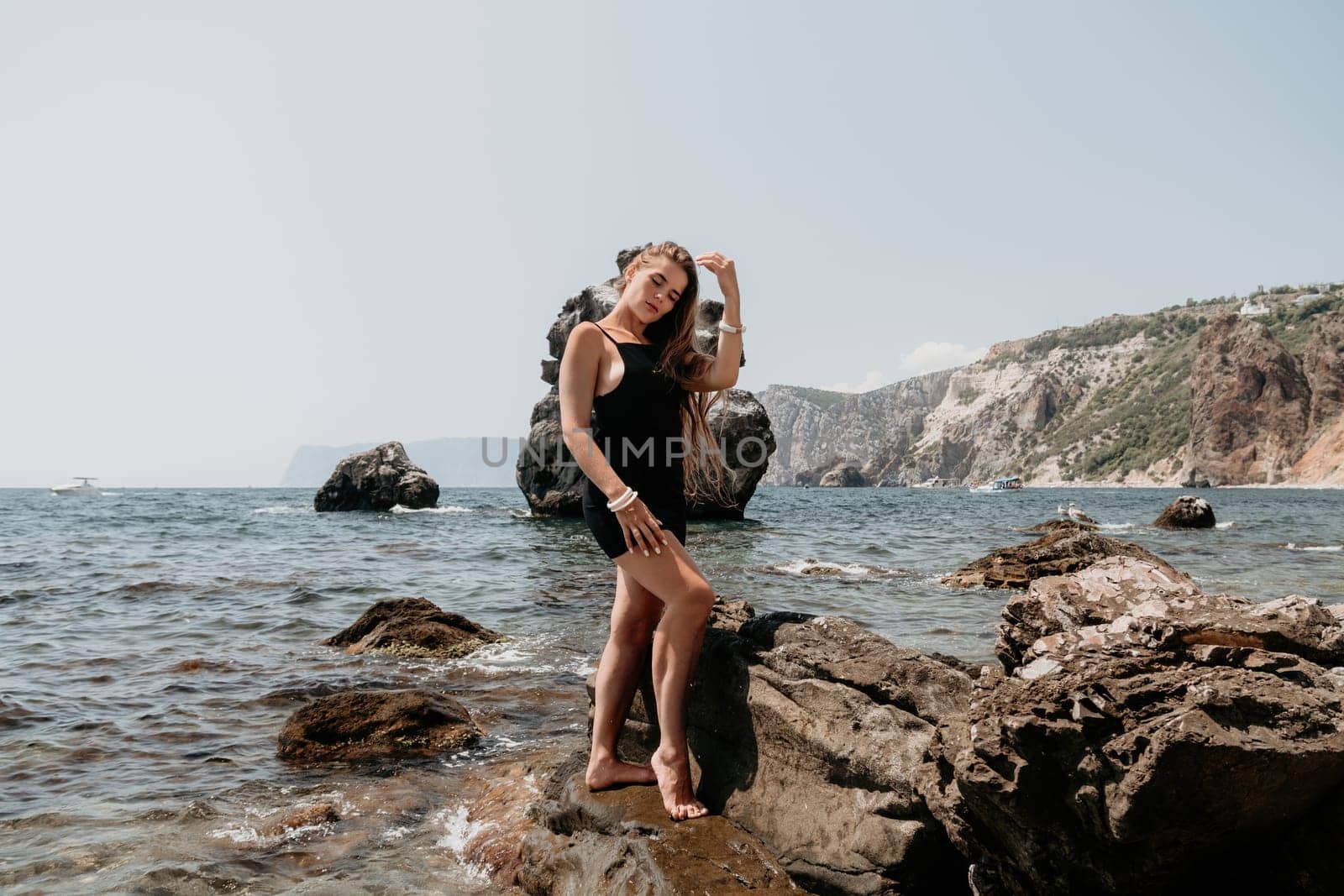 Woman travel sea. Young Happy woman in a long red dress posing on a beach near the sea on background of volcanic rocks, like in Iceland, sharing travel adventure journey