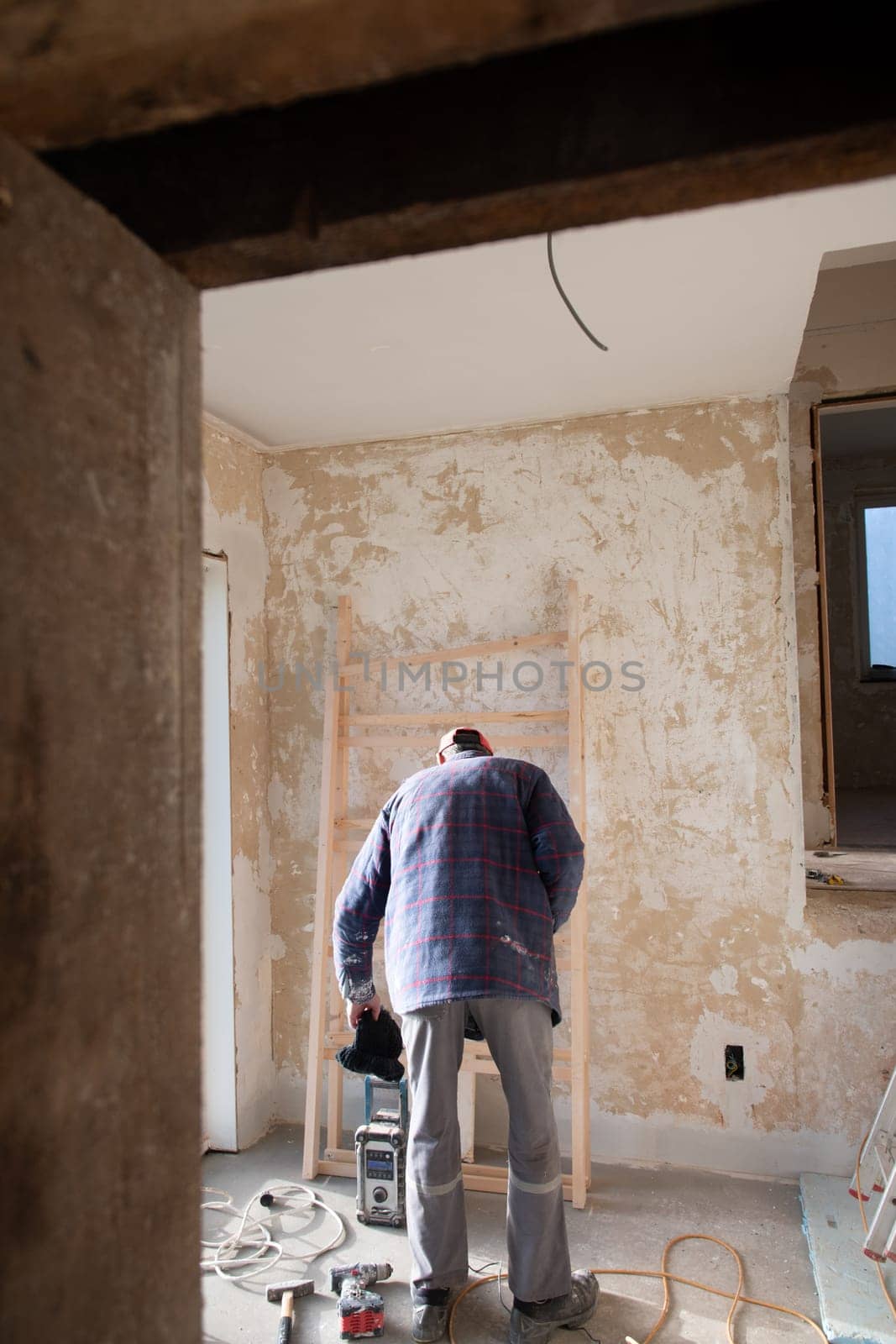 a male builder stands in an apartment near peeling walls and starts repairs in a new house in the middle of an empty room, High quality photo