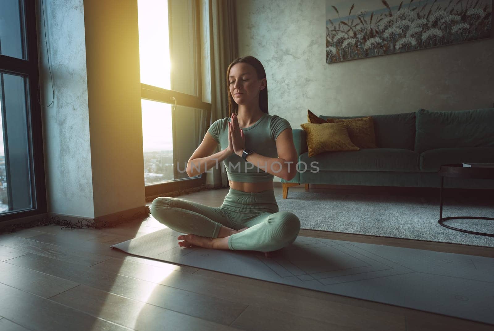 Woman practices yoga and meditates with eyes closed at home. Calmness and appeasement concept. Woman sitting in lotus pose. by DariaKulkova