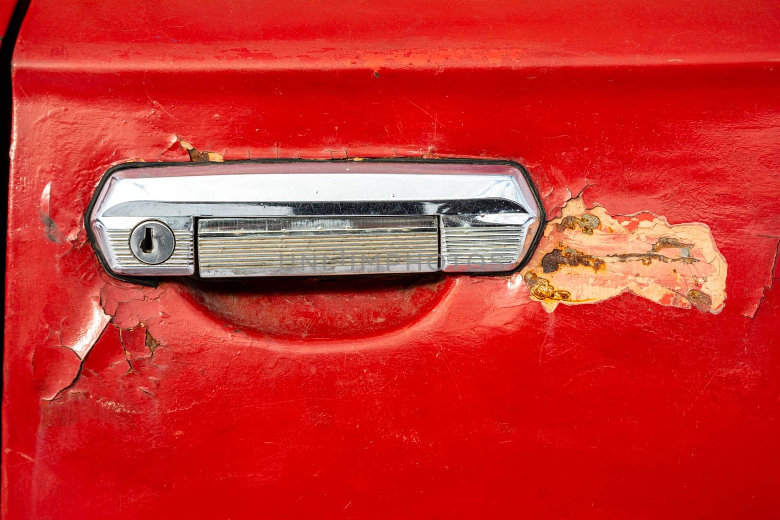 old car door handle close-up. The red door of an old car with a keyhole and peeling paint and putty