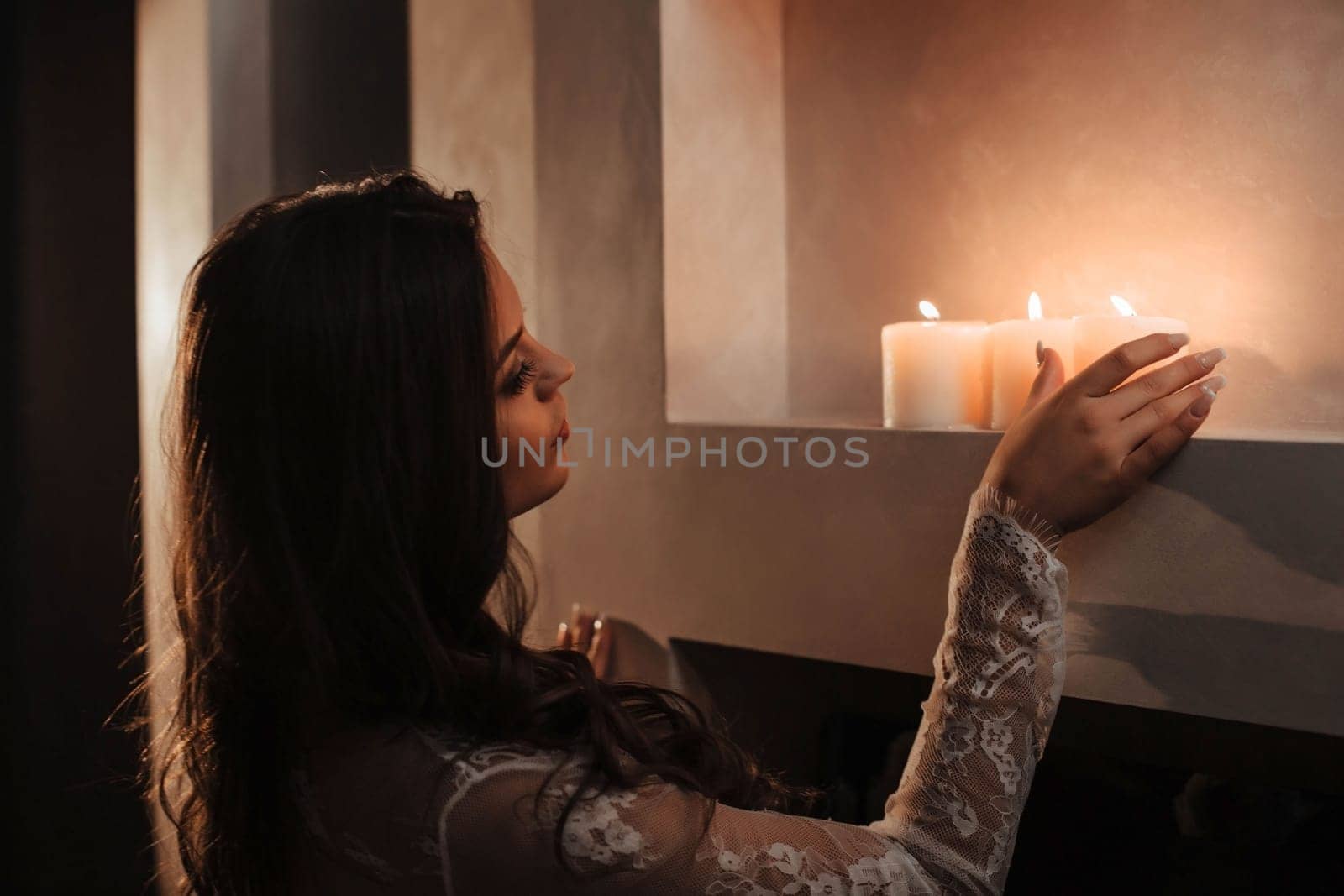 beautiful brunette in a white transparent tunic stands near the candles.
