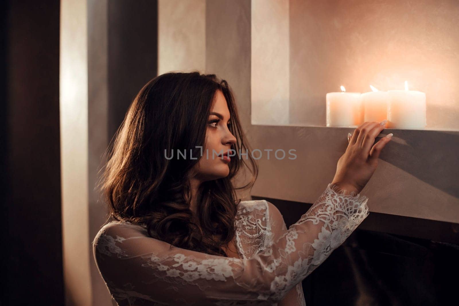 beautiful brunette in a white transparent tunic stands near the candles.