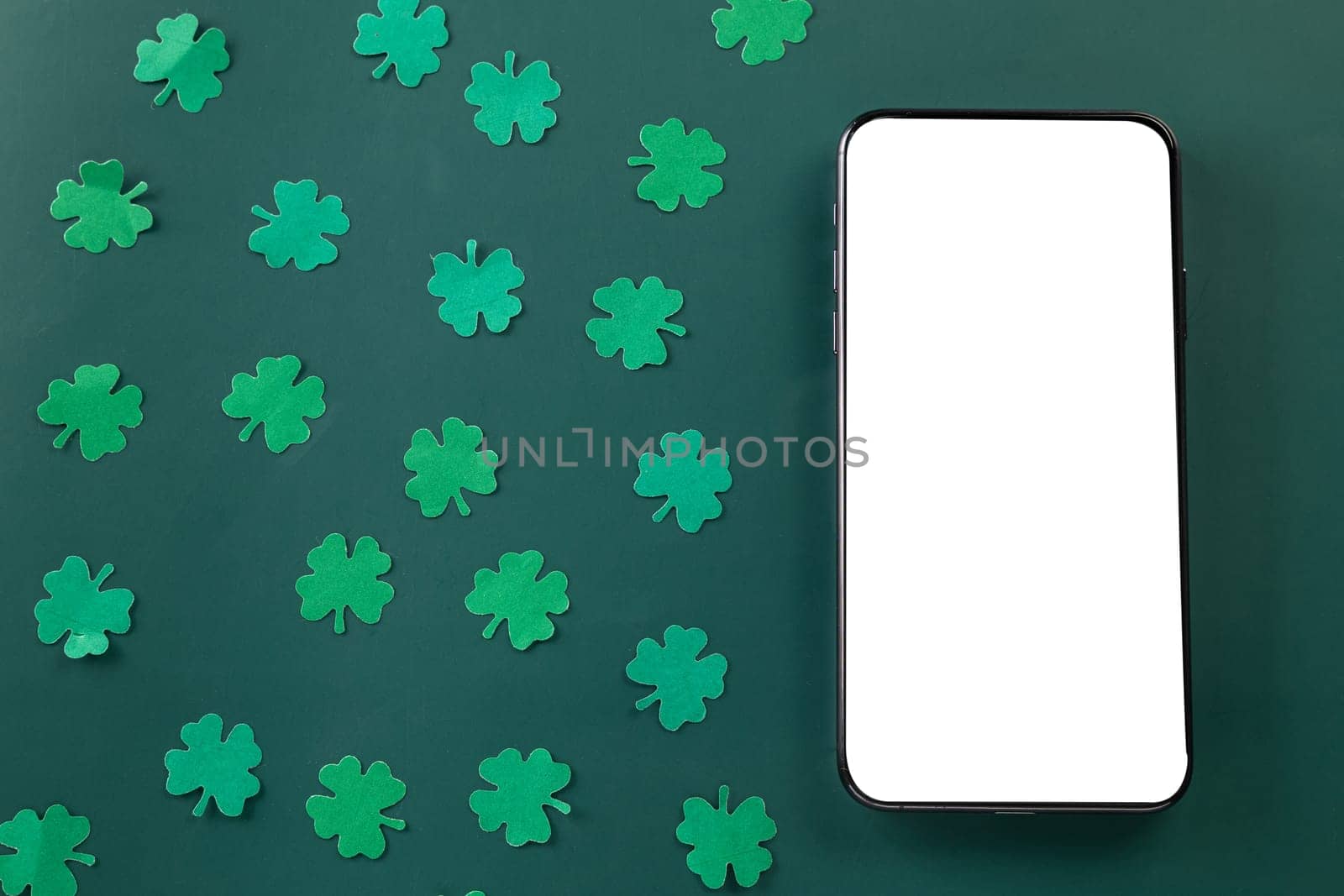 St Patricks Day. overhead flat lay of paper cut clover leaves festive decor and mobile phone blank screen, shamrocks leaf with smartphone holiday symbol on colour background, Banner greeting card