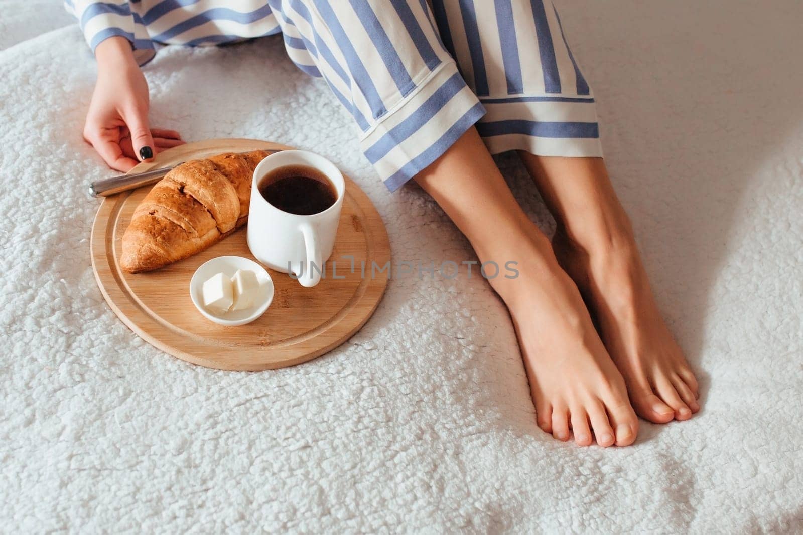 women's beautiful legs in pyjamas and next to a coffee with a croissant.the concept of coffee in bed . top view
