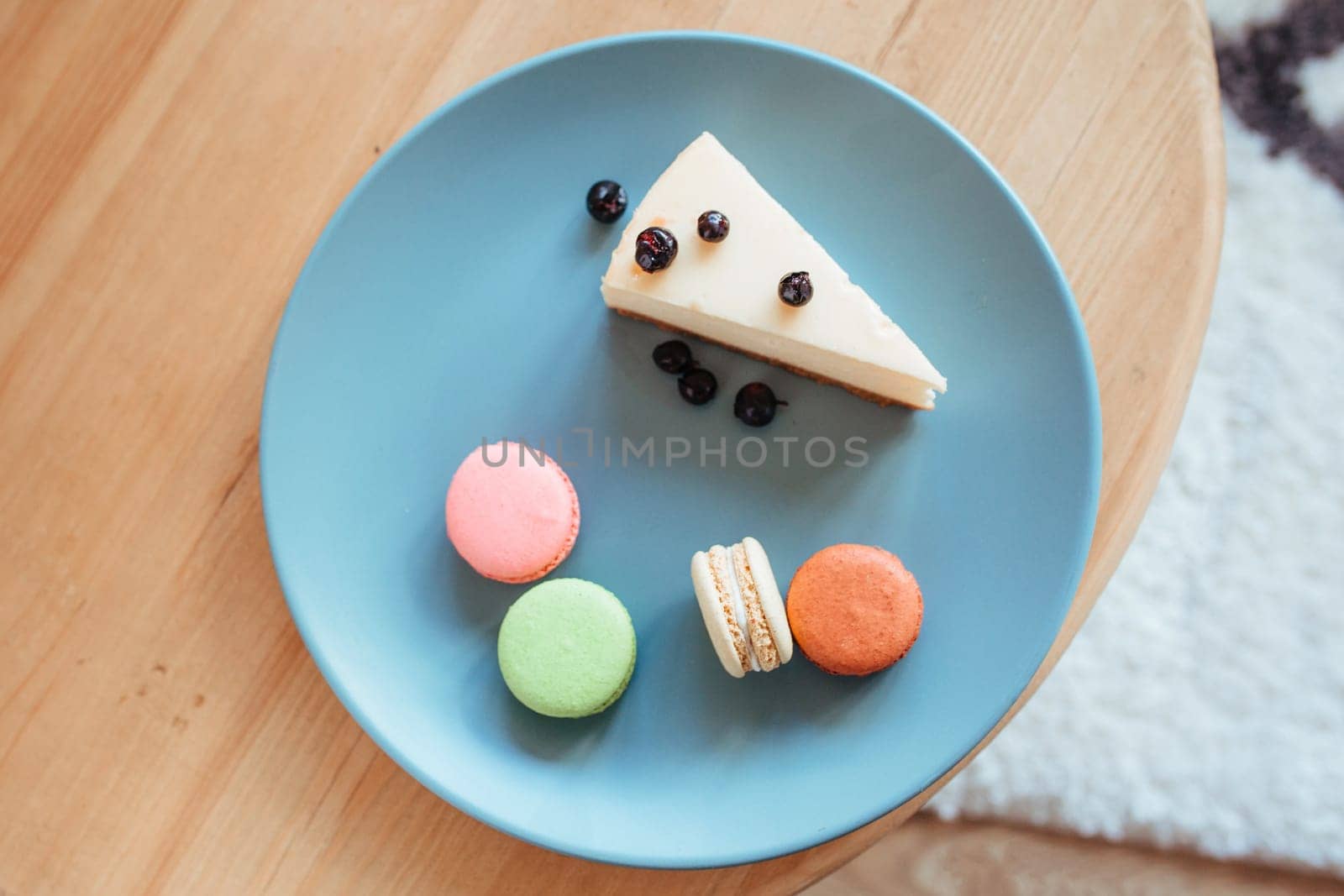 a cheese cake with blackcurrant and macarons on a turquoise plate sits on the edge of the coffee table. sweet breakfast concept