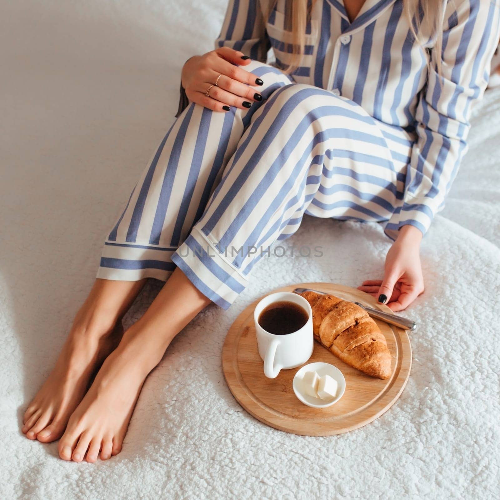 women's beautiful legs in pyjamas and next to a coffee with a croissant.the concept of coffee in bed . top view