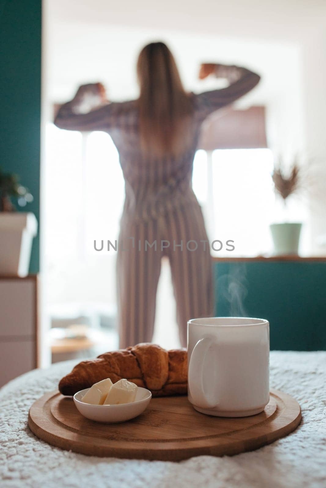 croissant and coffee in the foreground on the back of a girl in pyjamas. breakfast concept