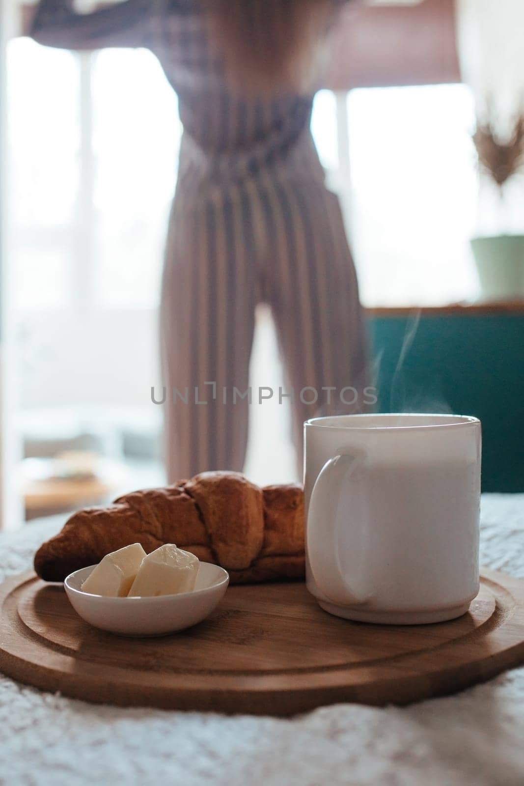 croissant and coffee in the foreground on the back of a girl in pyjamas. breakfast concept