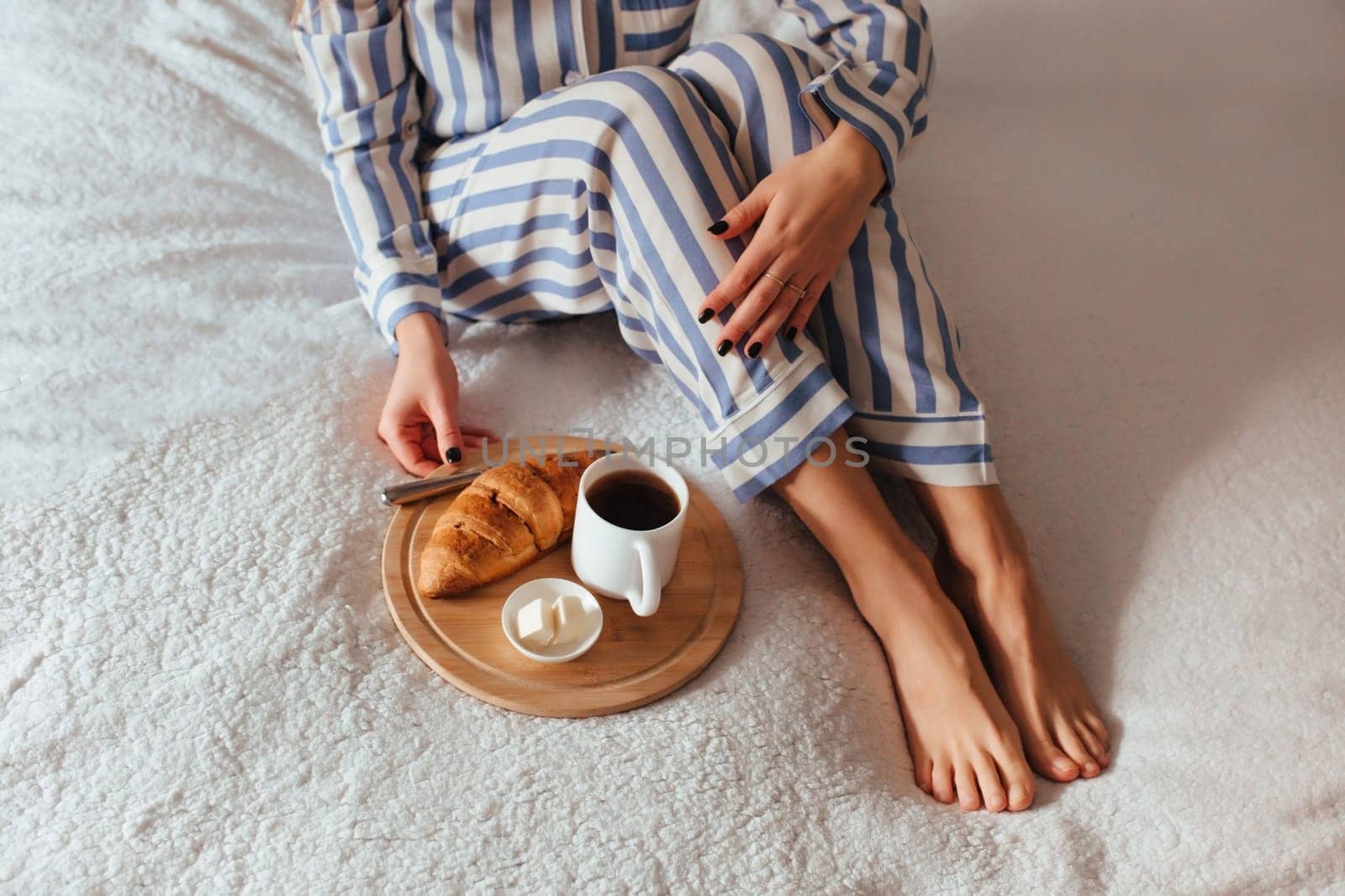 women's beautiful legs in pajamas and next to a coffee with a croissant.the concept of coffee in bed . top view