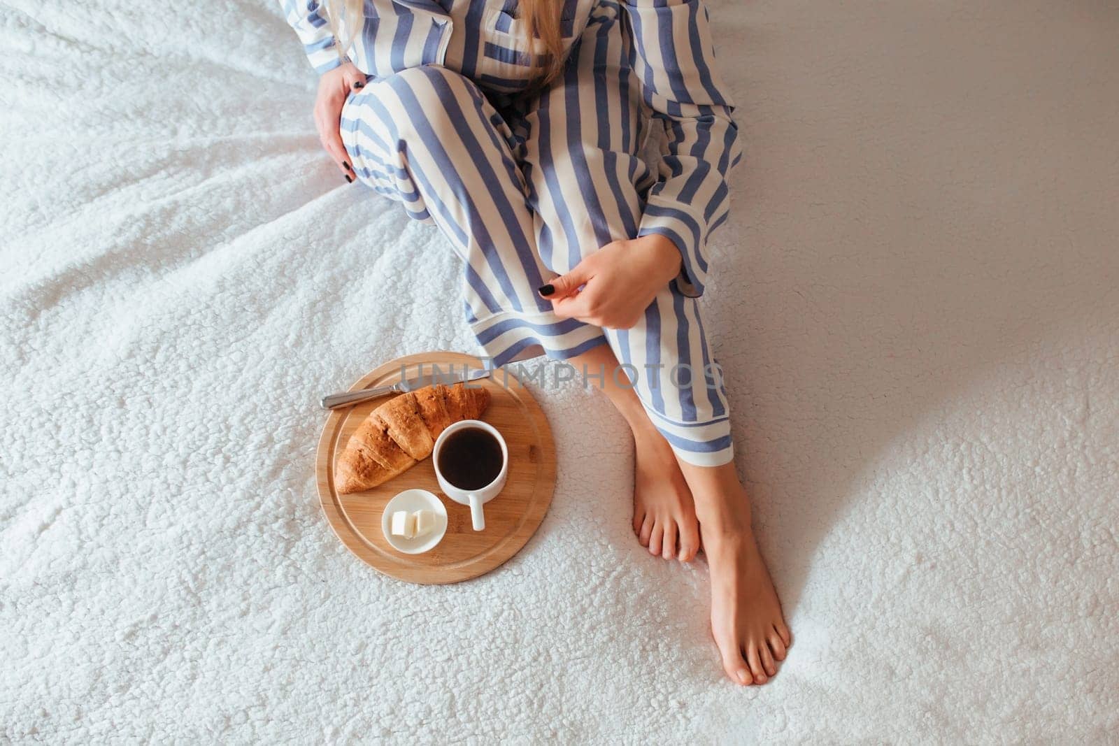 women's beautiful legs in pyjamas and next to a coffee with a croissant.the concept of coffee in bed . top view