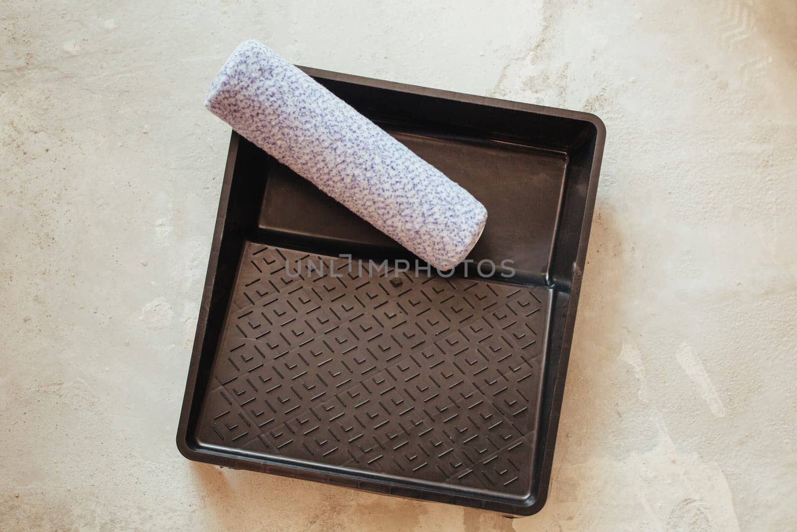 PAINT CONTAINER AND ROLLER TIP ON CONCRETE FLOOR