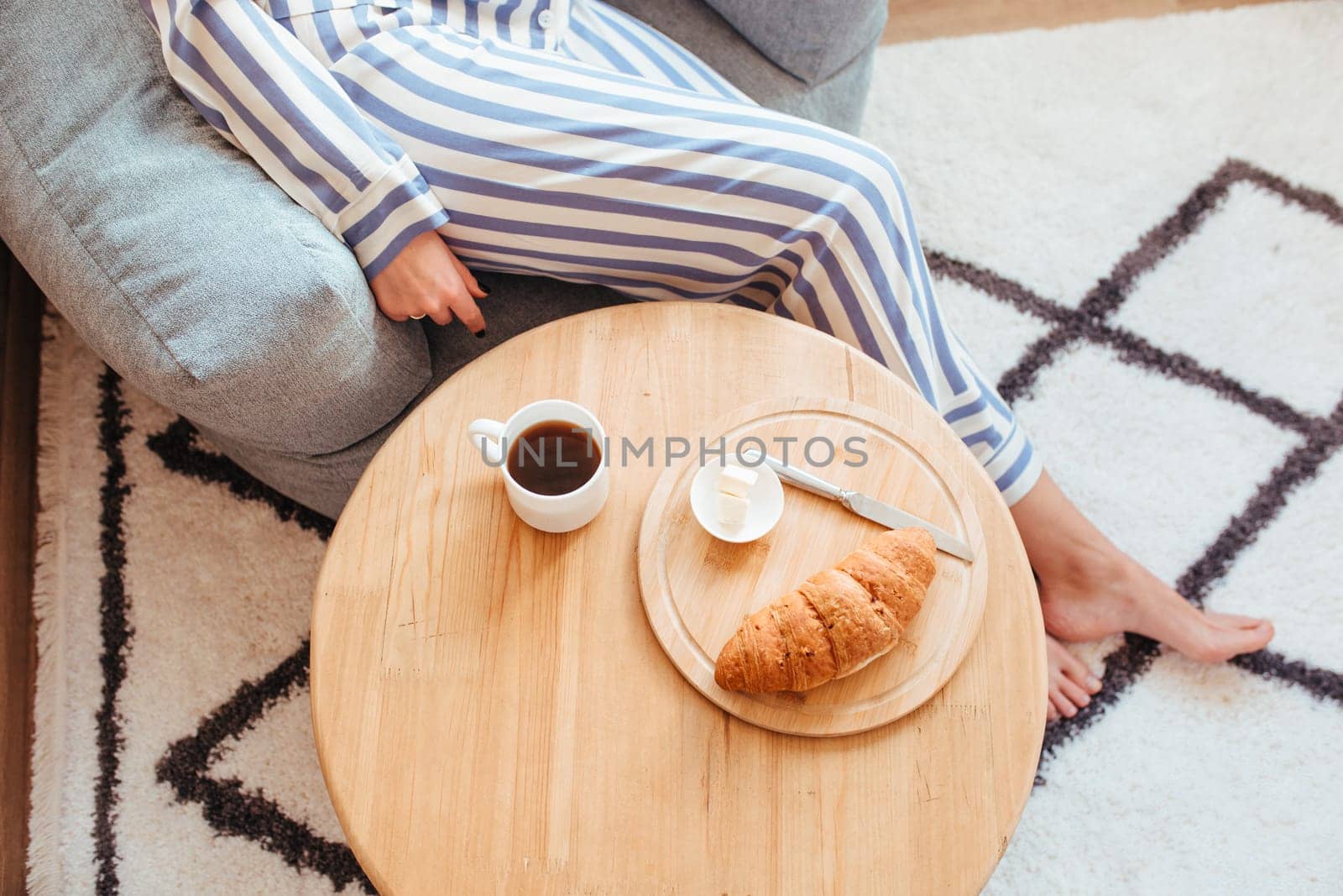 a woman in pajamas in the morning at a table drinks coffee and eats sweets cheesecake sweet macaroni . the concept of breakfast with sweets . top view