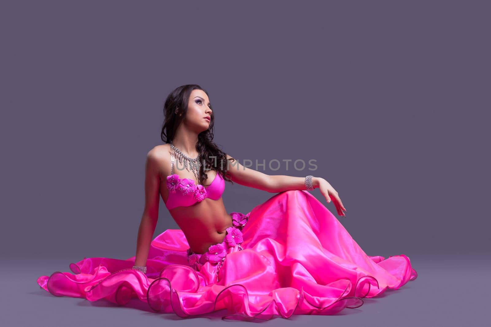 Full length portrait of pretty woman - dancer in oriental pink costume sitting on floor