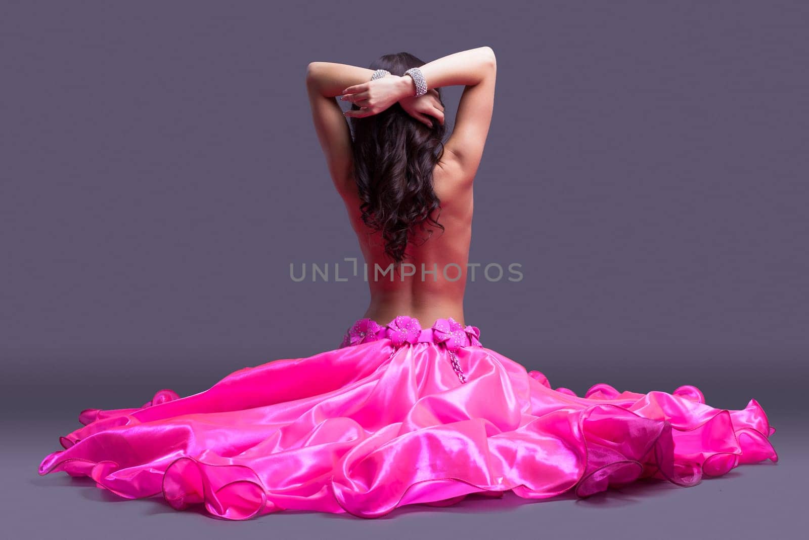 Studio portrait of dancer posing topless in pink costume sitting on floor