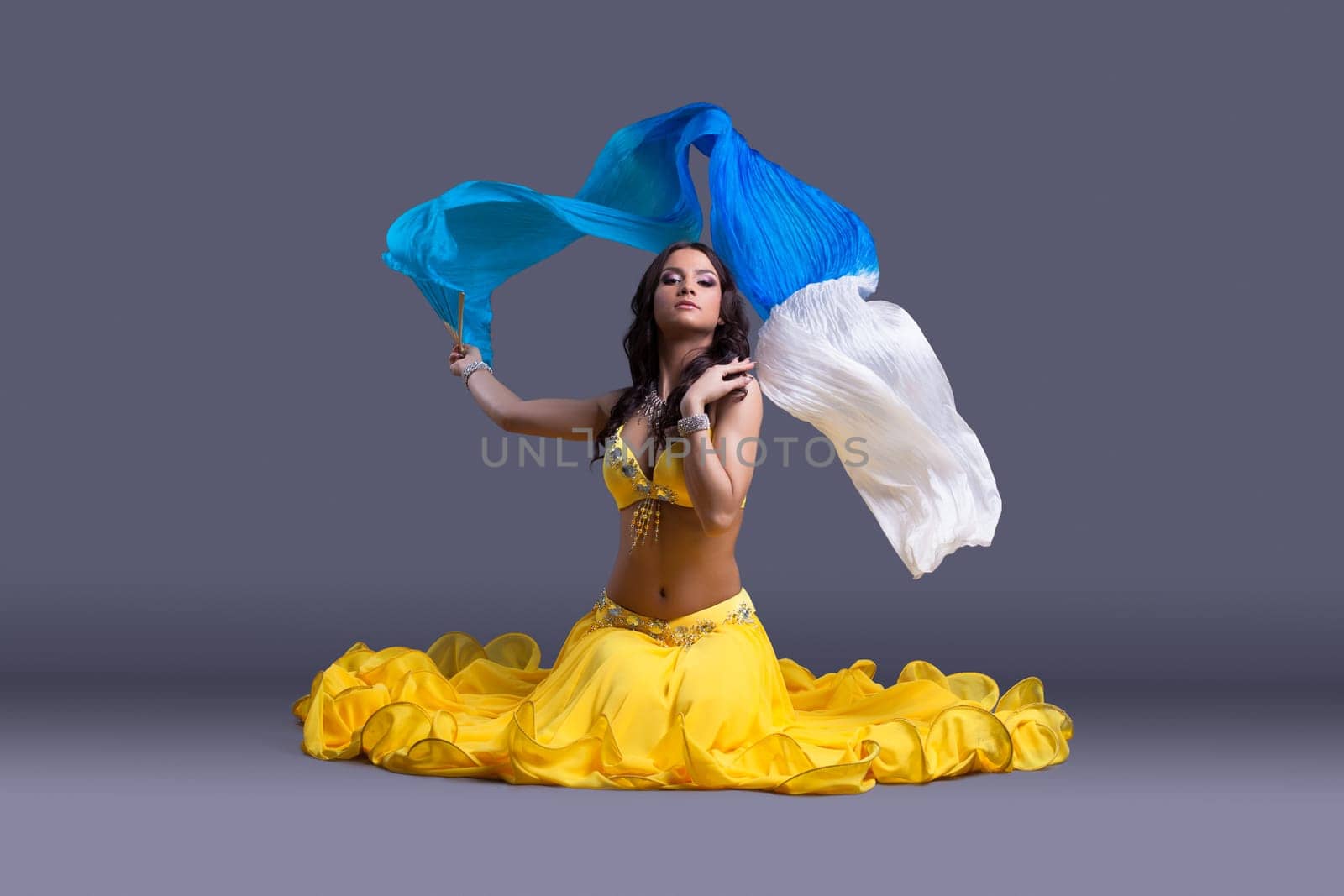 Full length portrait of pretty dancer in yellow costume sitting on floor