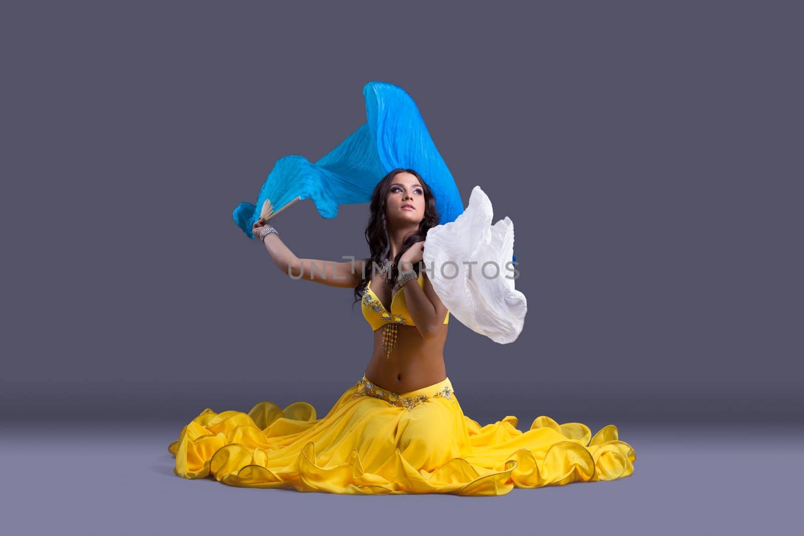 Full length portrait of beautiful dancer in yellow costume sitting on floor