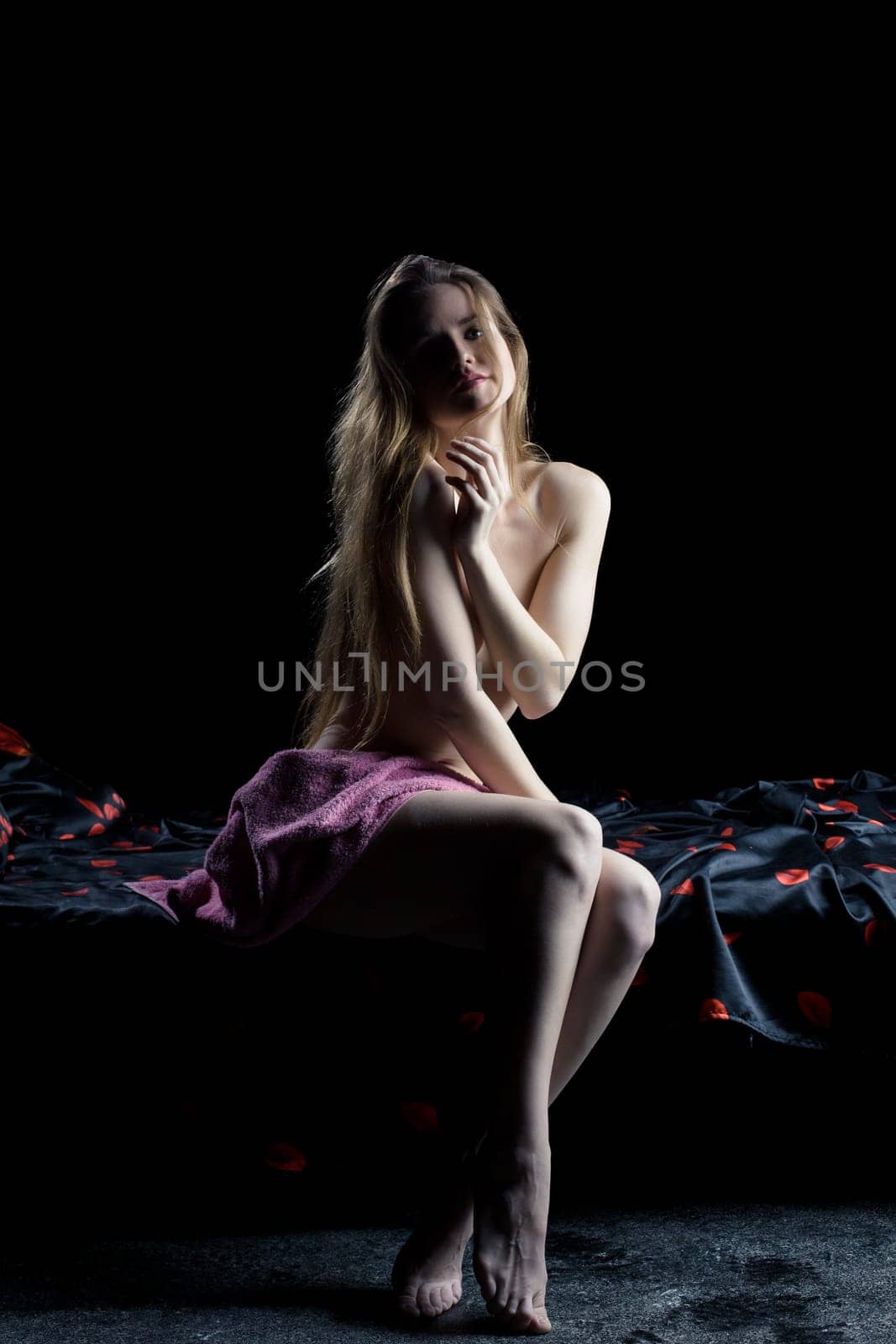 Full length portrait of beautiful young woman sitting on bed in dark bedroom